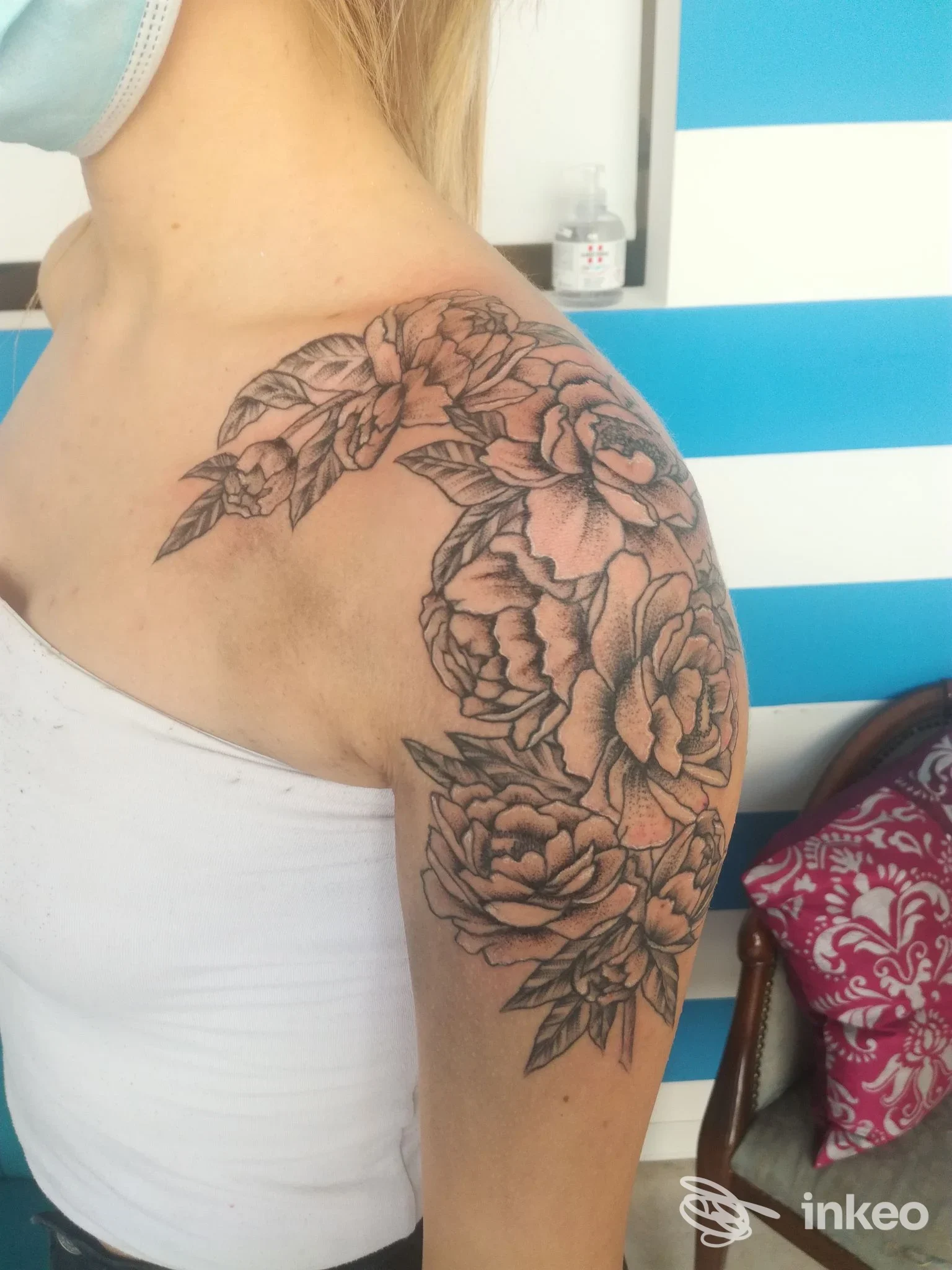 Tattoo floreale estesa sulla spalla e parte superiore del braccio, disegnata a linee e sfumature nere, visibile sulla pelle della persona senza mostrare il viso.
