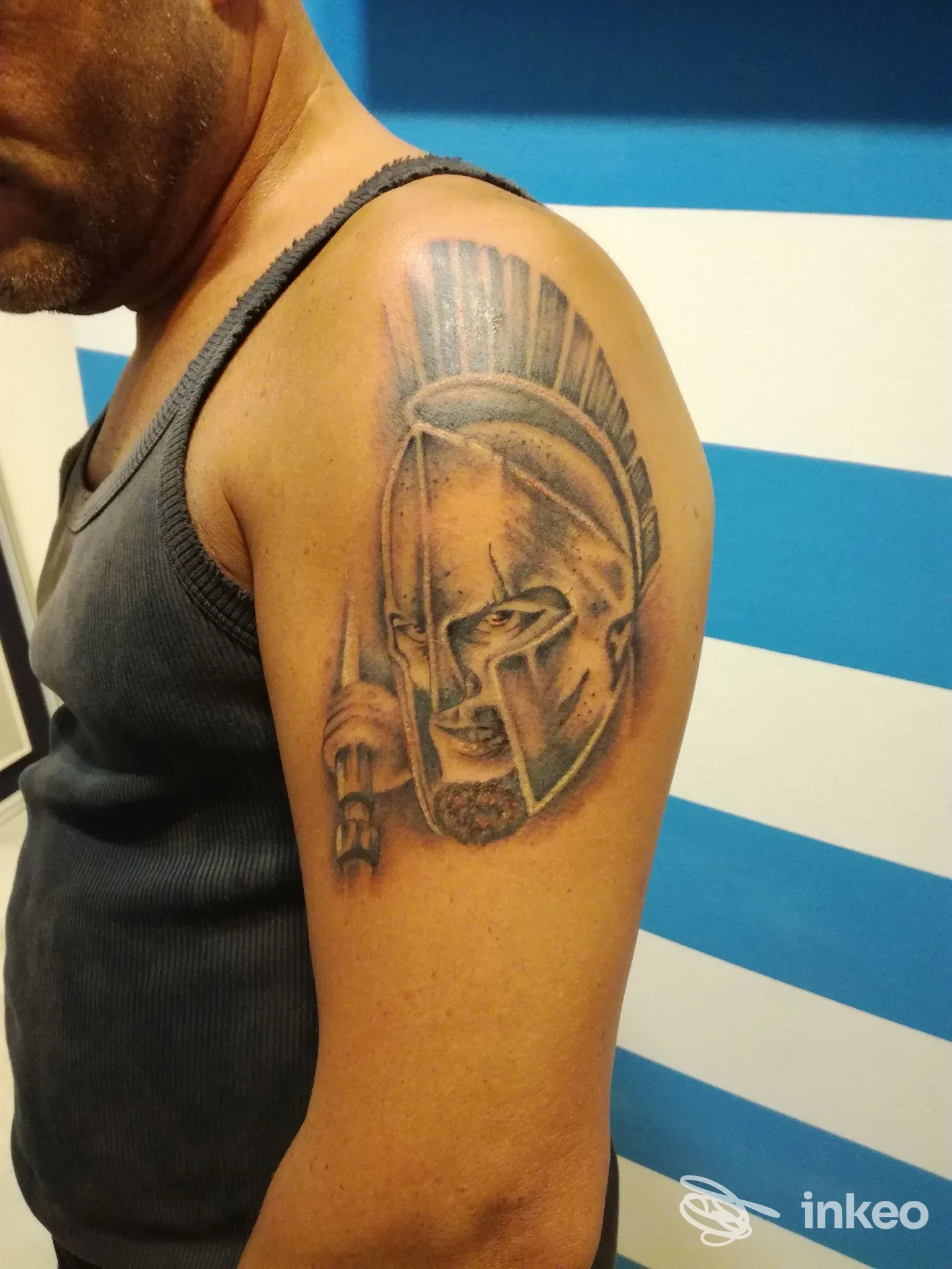 Tattoo visibile sull’avambraccio di un uomo: elmo stilizzato con linee scure e dettagli, tono della pelle visibile.