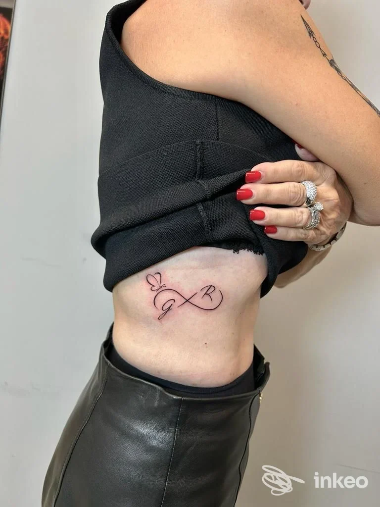 Tatuaggio a forma di infinito con iniziali e piccolo cuore sul fianco, lavoro fotografato da INK HOUSE TATTOO DI FAZIO GABRIELE a Barcellona Pozzo di Gotto.