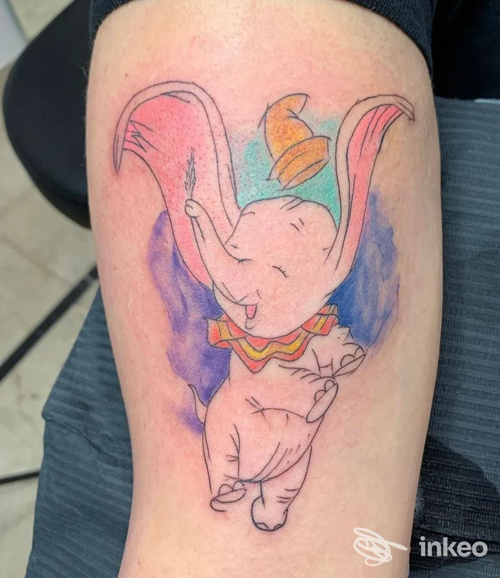 Tatuaggio colorato a tema elefantino realizzato da Inked Tattoo, Vittoria, su pelle della coscia con sfondo acquerello.