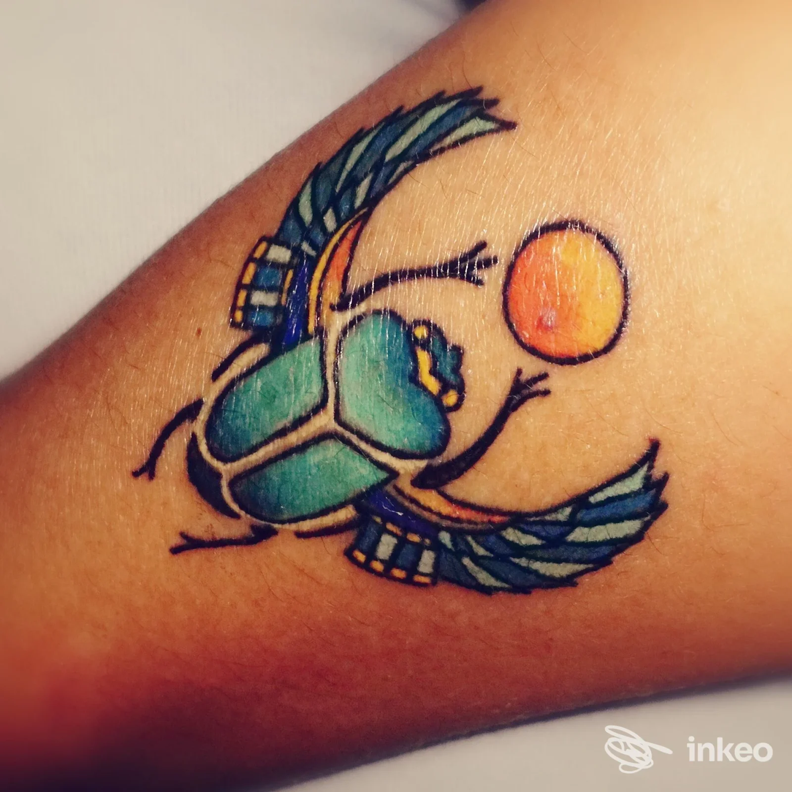 Tatuaggio di uno scarabeo alato con sfera arancione sull'avambraccio, immagine fornita da L'Alfiere Tattoo a Lentini.
