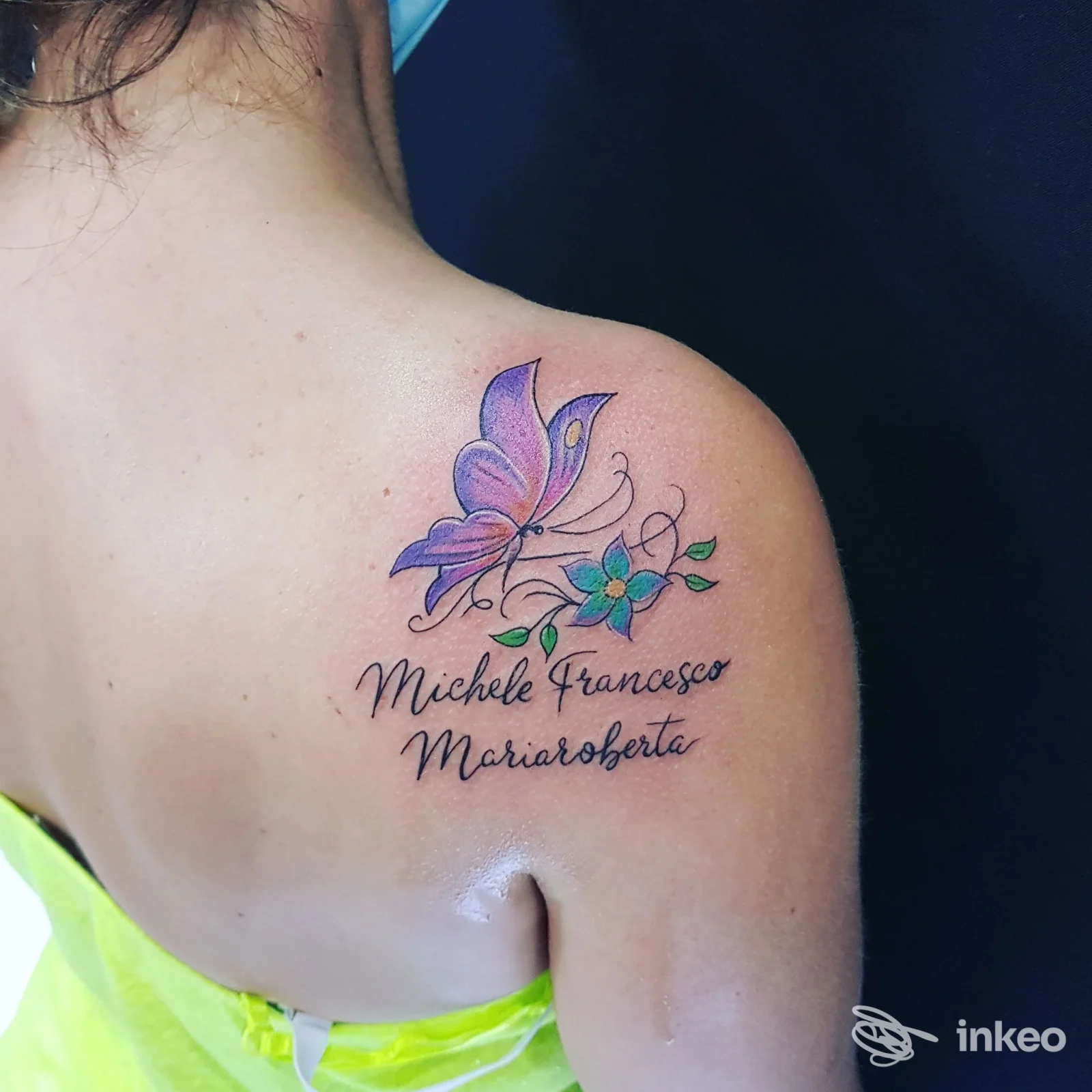 Tatuaggio colorato su spalla/scapola con farfalla e nomi, foto dello studio LINEEDINKIOSTRO TATTOO a Villarosa.