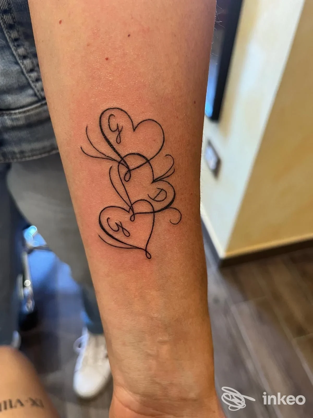 Fotografia di un tatuaggio lineare su avambraccio con tre cuori intrecciati, eseguito da Jolly Roger Tattoo a San Giuseppe Jato.