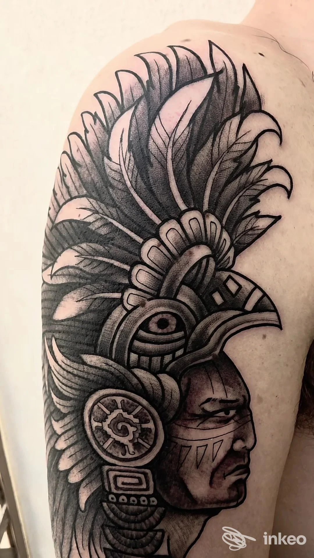 Grande tatuaggio a inchiostro nero e grigio su spalla e braccio superiore, ritratto con copricapo piumato – L' Arte del Tattoo da Fabio Ingrassia, Marsala