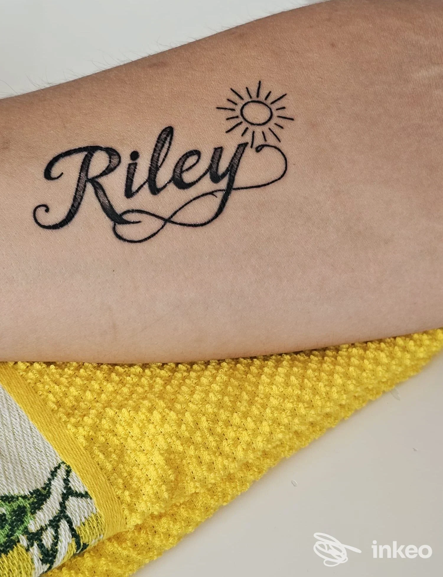 Tatuaggio con scritta 'Riley' e sole stilizzato sull'avambraccio, MaiMuni tattoo studio a Santa Teresa di Riva.