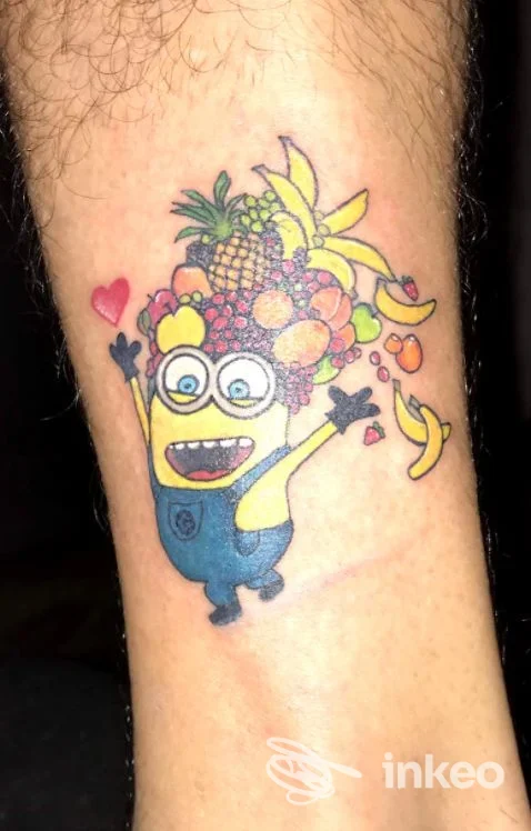 Tatuaggio colorato su polpaccio raffigurante un personaggio in stile cartoon con una corona di frutta. Maieutica studio di Yole tattoo art, Palermo.