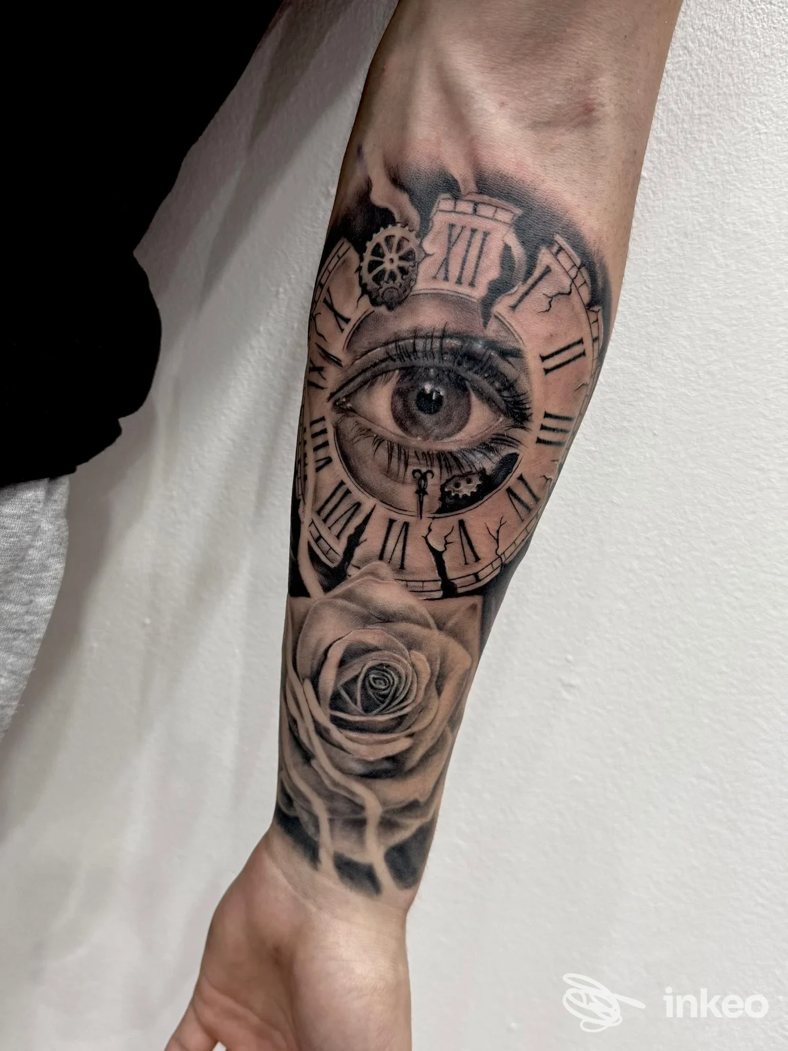 Tatuaggio realistico su avambraccio con occhio dettagliato, quadrante d'orologio frantumato e rosa, realizzato da Mammut Tattoo Srl a Siracusa.