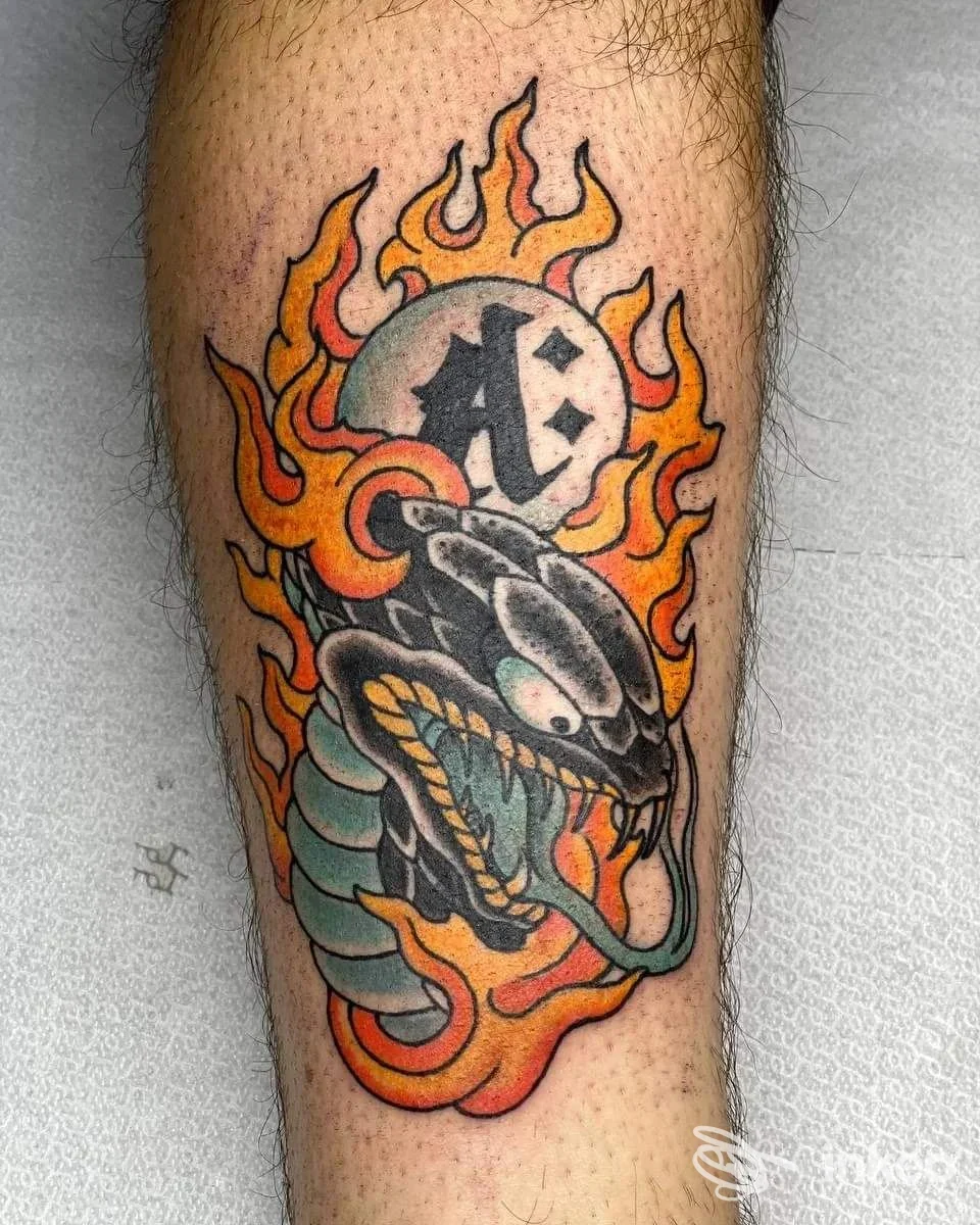 Tatuaggio su polpaccio raffigurante testa di serpente tra fiamme e globo con lettere, fotografia inviata da Mutazioni Tattoo, Catania.