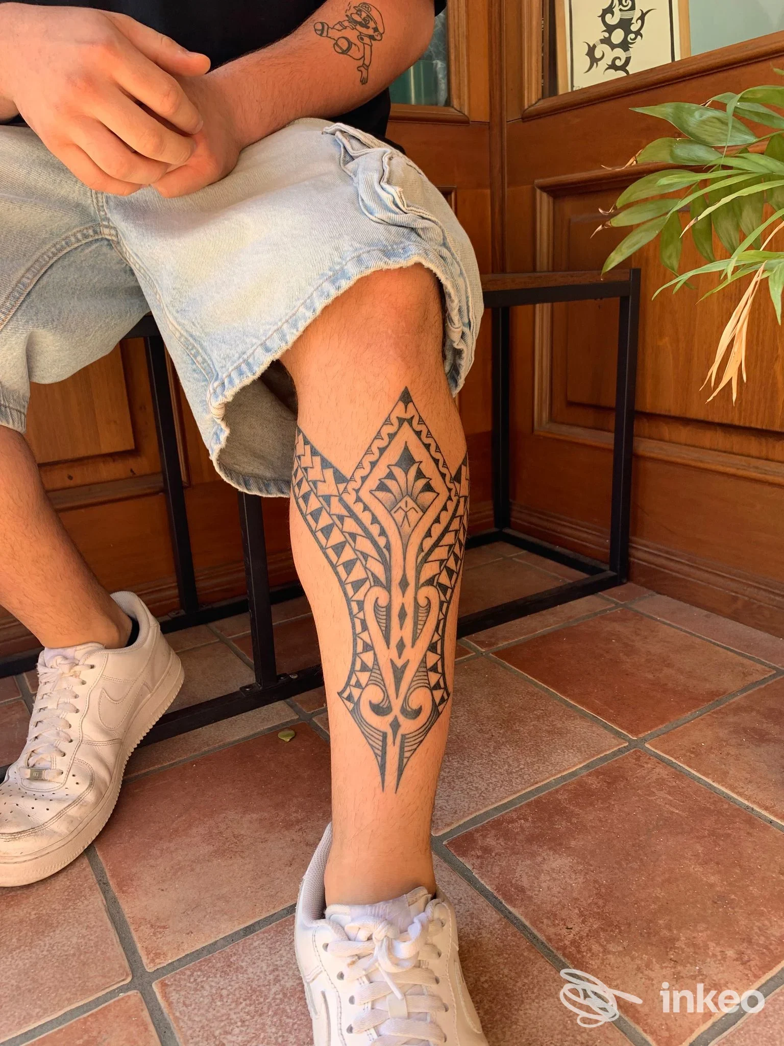 Tatuaggio nero stilizzato sullo stinco sinistro fotografato seduto, immagine dallo studio Old iron tattoo shop a Bagheria.