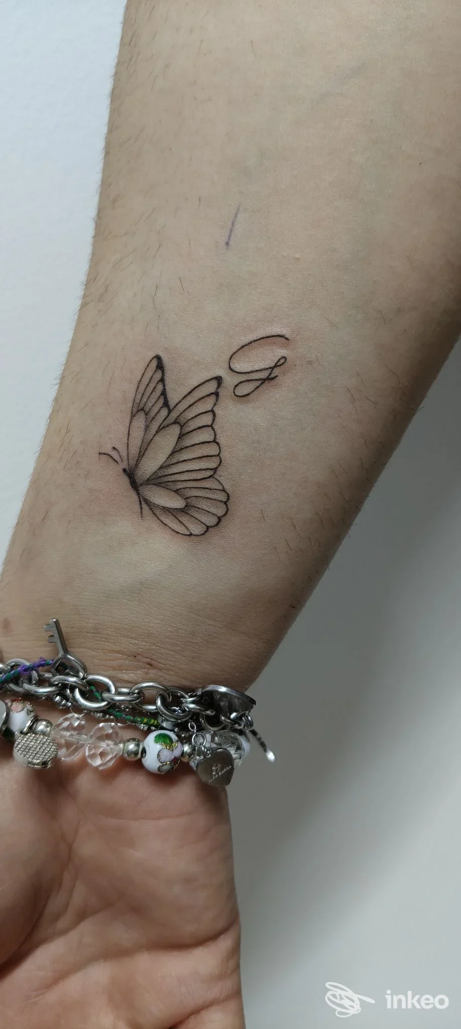 Tatuaggio farfalla delicata con una lettera 'G' sul polso/avambraccio, eseguito da Putìa Tattoo di Aurelio Trapani a Marsala.
