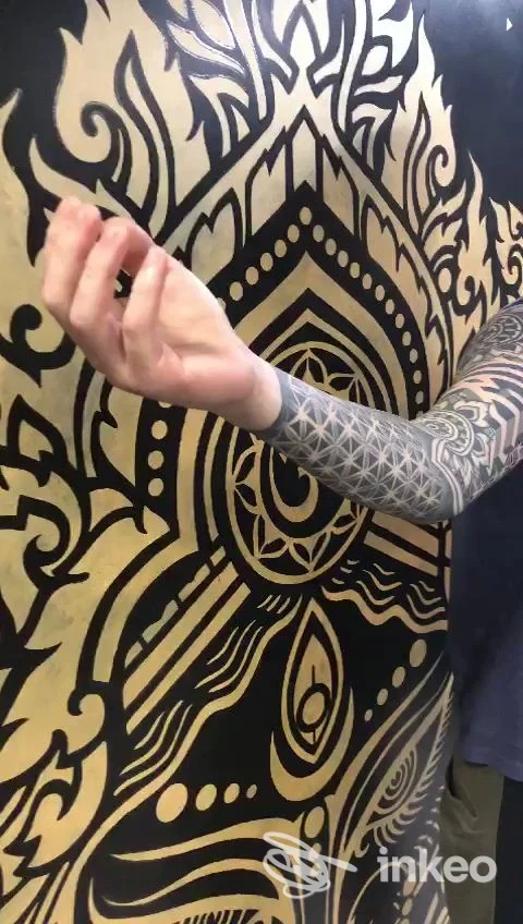 Manica tatuata geometrica su avambraccio fotografata davanti a un grande murale; Red Home TATTOO, Aci Catena.