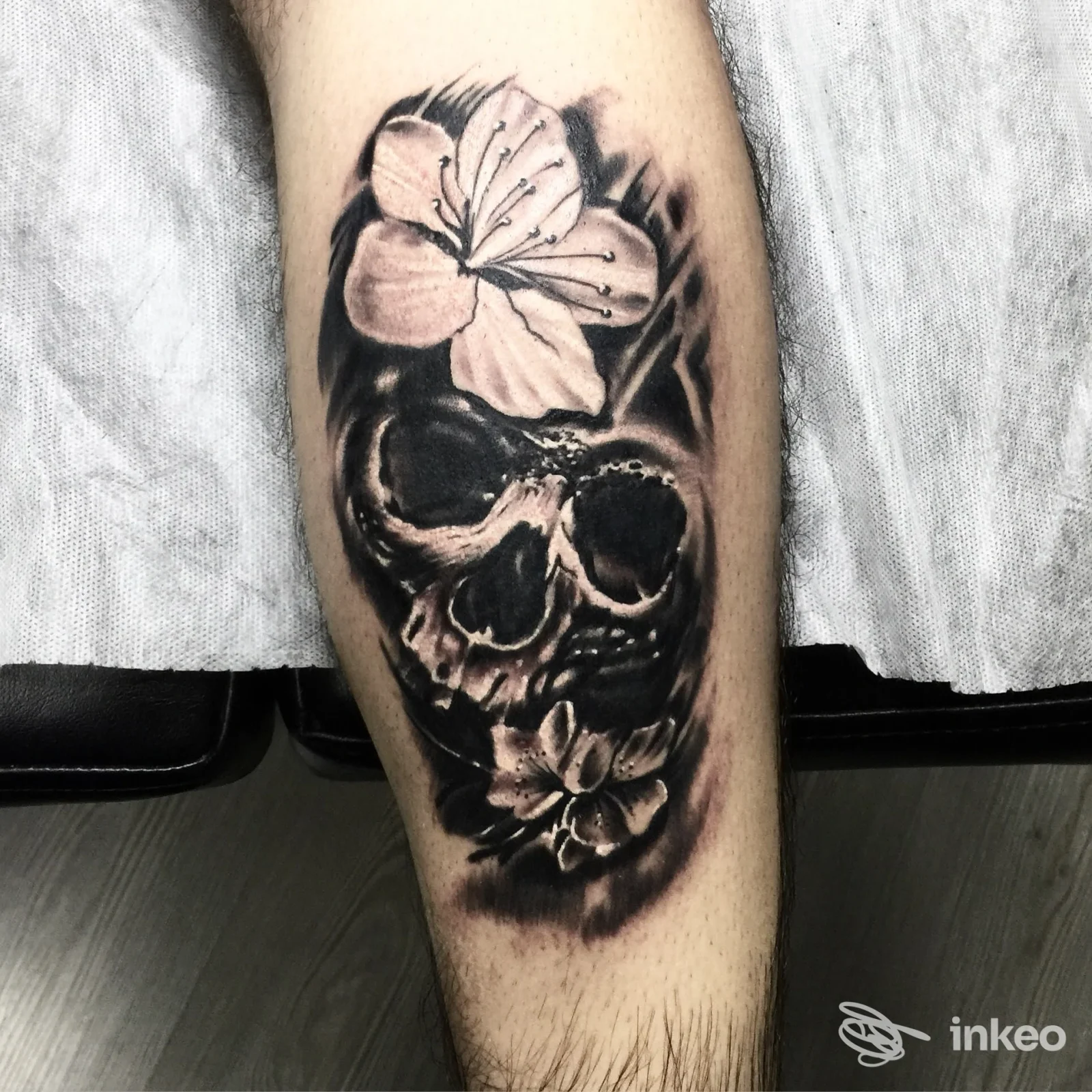 Tatuaggio realistico di teschio con fiori sul polpaccio, sfumato in nero e grigio — Rediamond Tattoo, Messina.