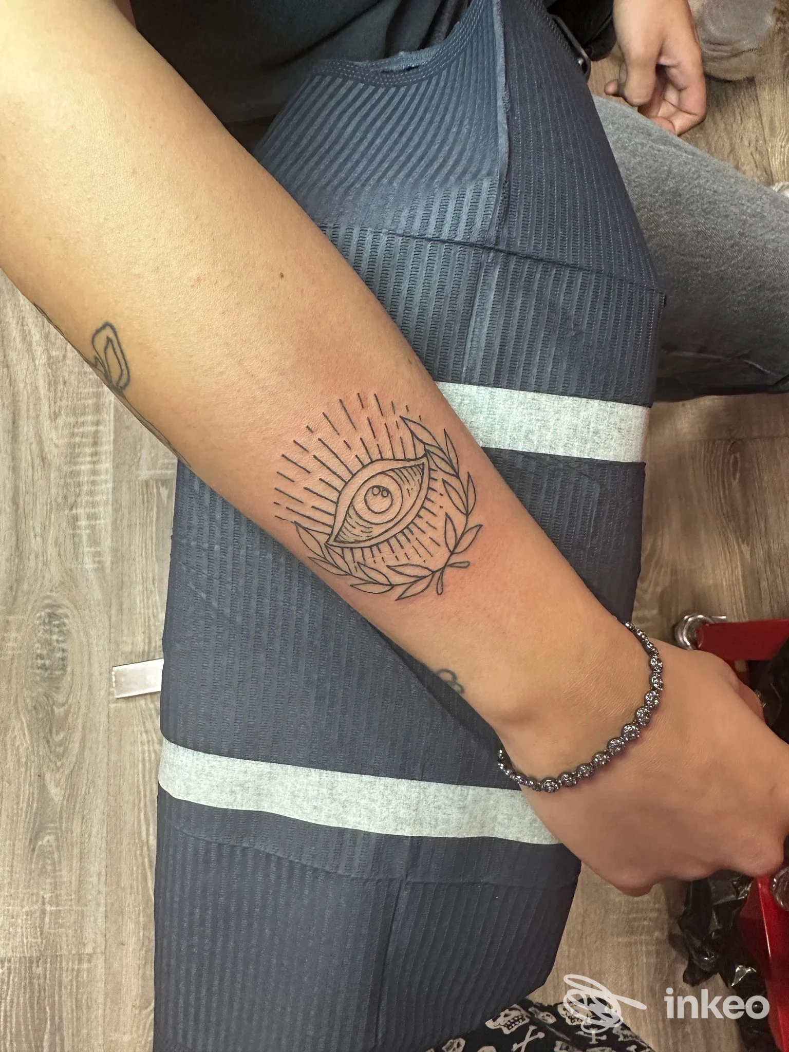 Foto di un tatuaggio sull'avambraccio: occhio stilizzato con raggi e foglie. Plh’s factory - Piazza Armerina.