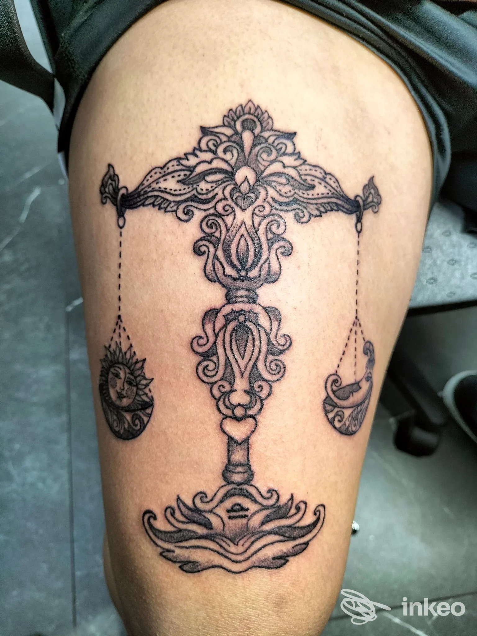 Tatuaggio ornamentale a inchiostro nero raffigurante una bilancia sulla coscia. Shades Ink Tattoo, Aci Castello.