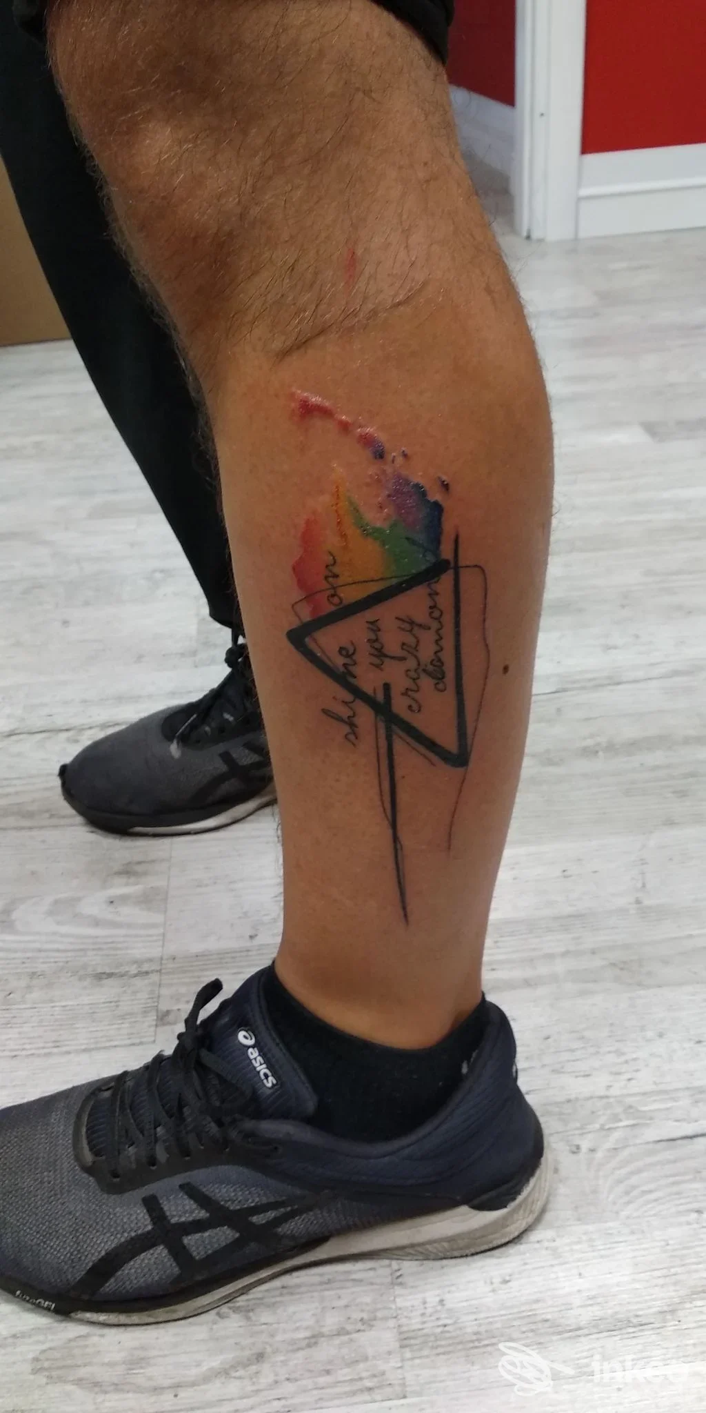 Tatuaggio geometrico a triangolo con arco cromatico su gamba, tratto nero e colori vivaci, realizzato direttamente sulla pelle.