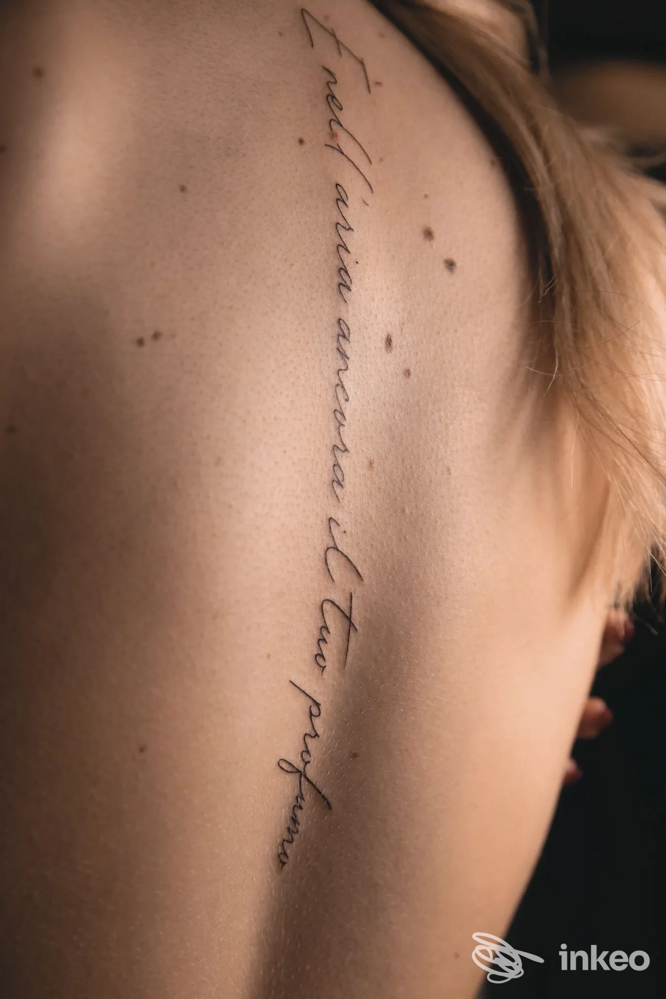 Tattoo verticale in corsivo su pelle reale lungo la schiena, visibile da lato; nessun volto presente, senza overlay o schermo.