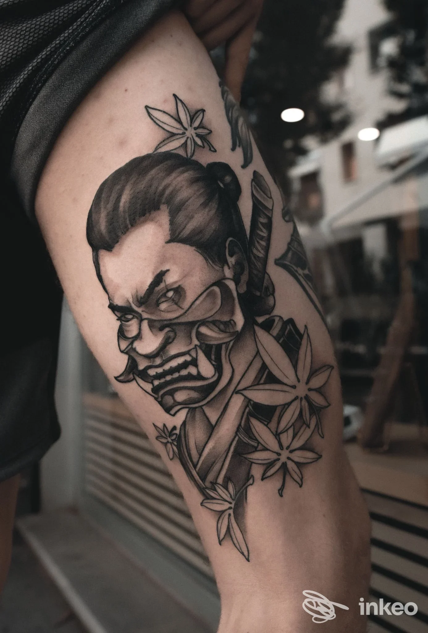 Tatuaggio in bianco e nero su pelle scoperta: ritratto stilizzato di un uomo con espressione severa, accompagnato da fiori; disegno visibile sul braccio superiore.