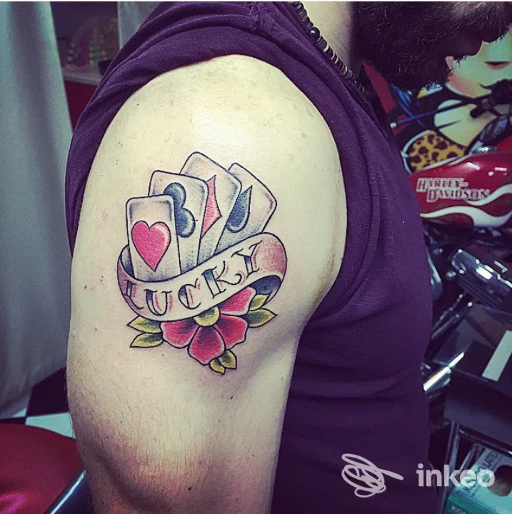 Tatuaggio sul deltoide con carte, nastro 'LUCK' e fiore, Skin Tattoo di La Rocca Adriano, Giardini-Naxos.