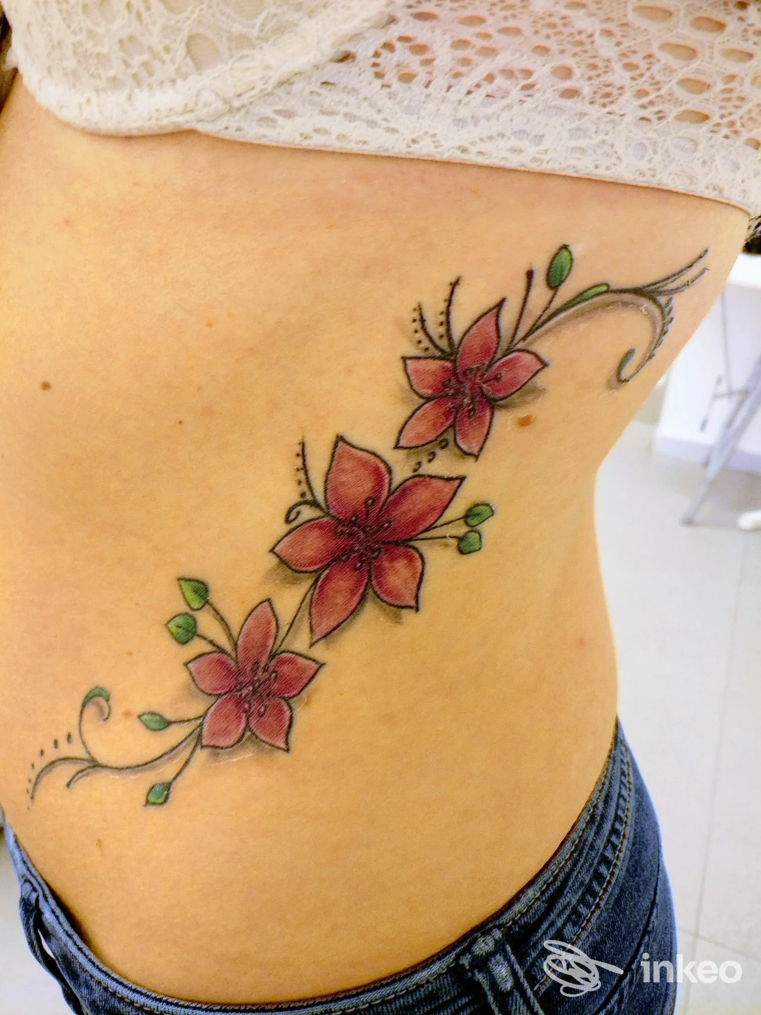 Tatuaggio floreale sul fianco con tre fiori rossi e foglie verdi, scatto nello studio Soho Tattoo di Fabio La China a Palermo.