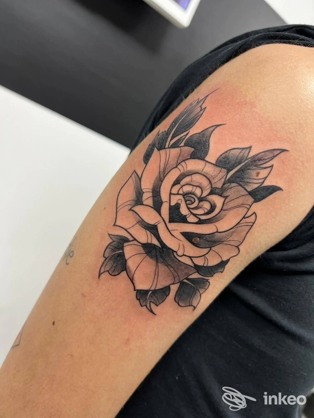 Tatuaggio a rosa in nero e grigio sul braccio superiore di una persona, eseguito da Spinelli’s Tattoo a Palma di Montechiaro, dettaglio ravvicinato.