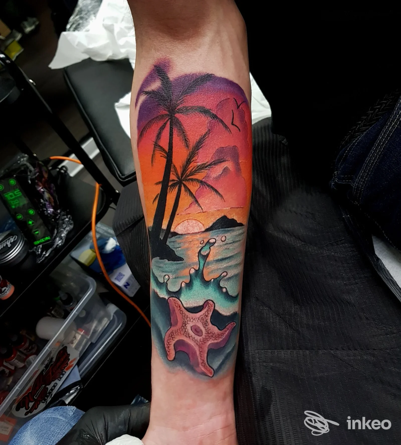 Tatuaggio a colori su avambraccio raffigurante tramonto tropicale con palme, onde e stella marina. Scatto da Spaceinktattoo, Milazzo.