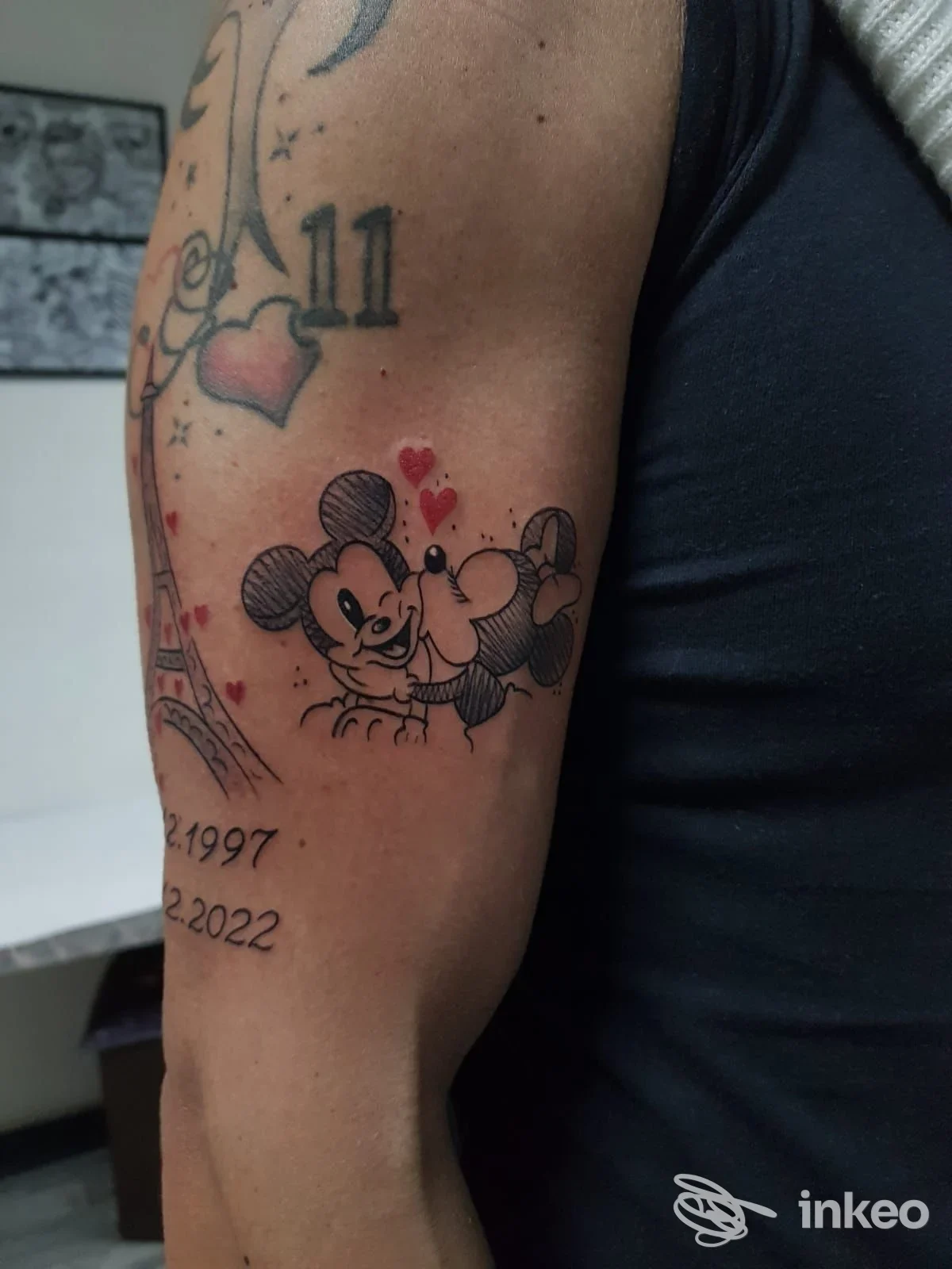 Tatuaggio a colori sul braccio superiore con due personaggi in stile cartoon e piccoli cuori, Tattoo Evolution, Giarre.