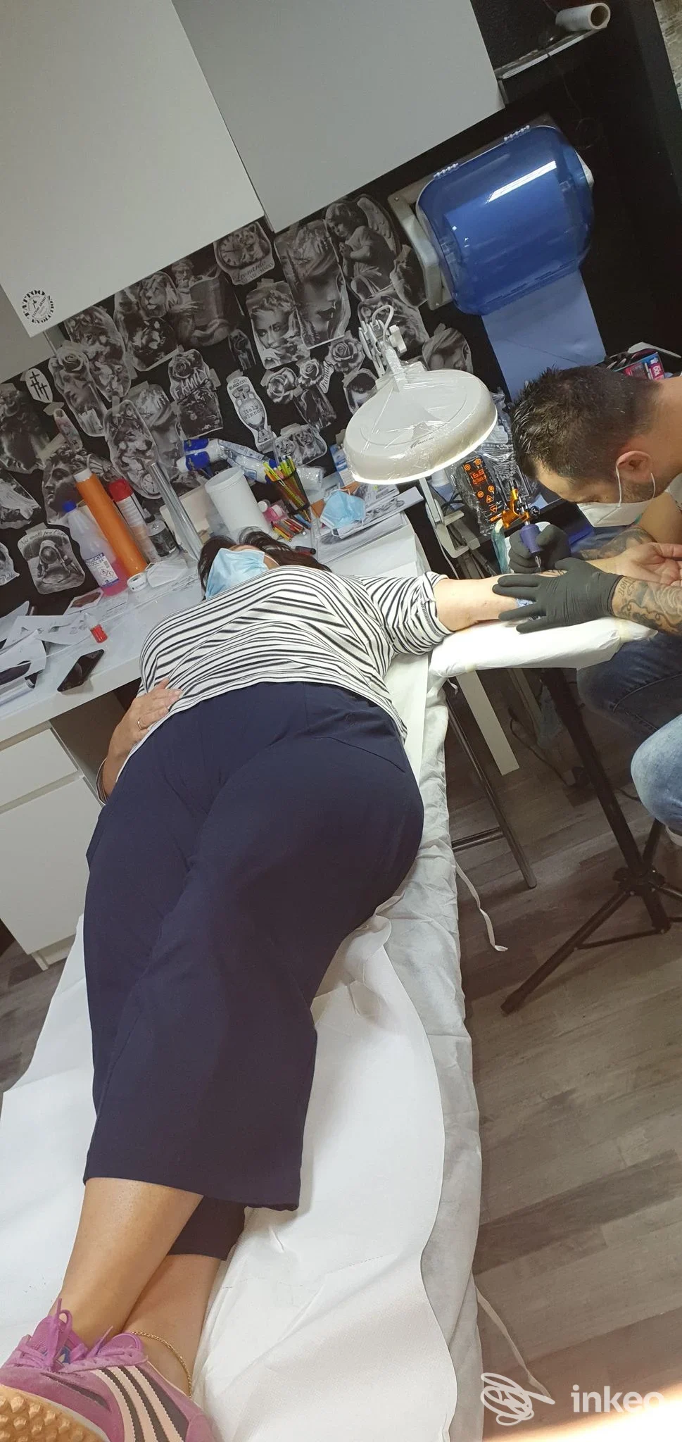 Cliente sdraiata su un lettino mentre il tatuatore lavora sull'avambraccio nello studio Tattoo Evolution a Giarre.