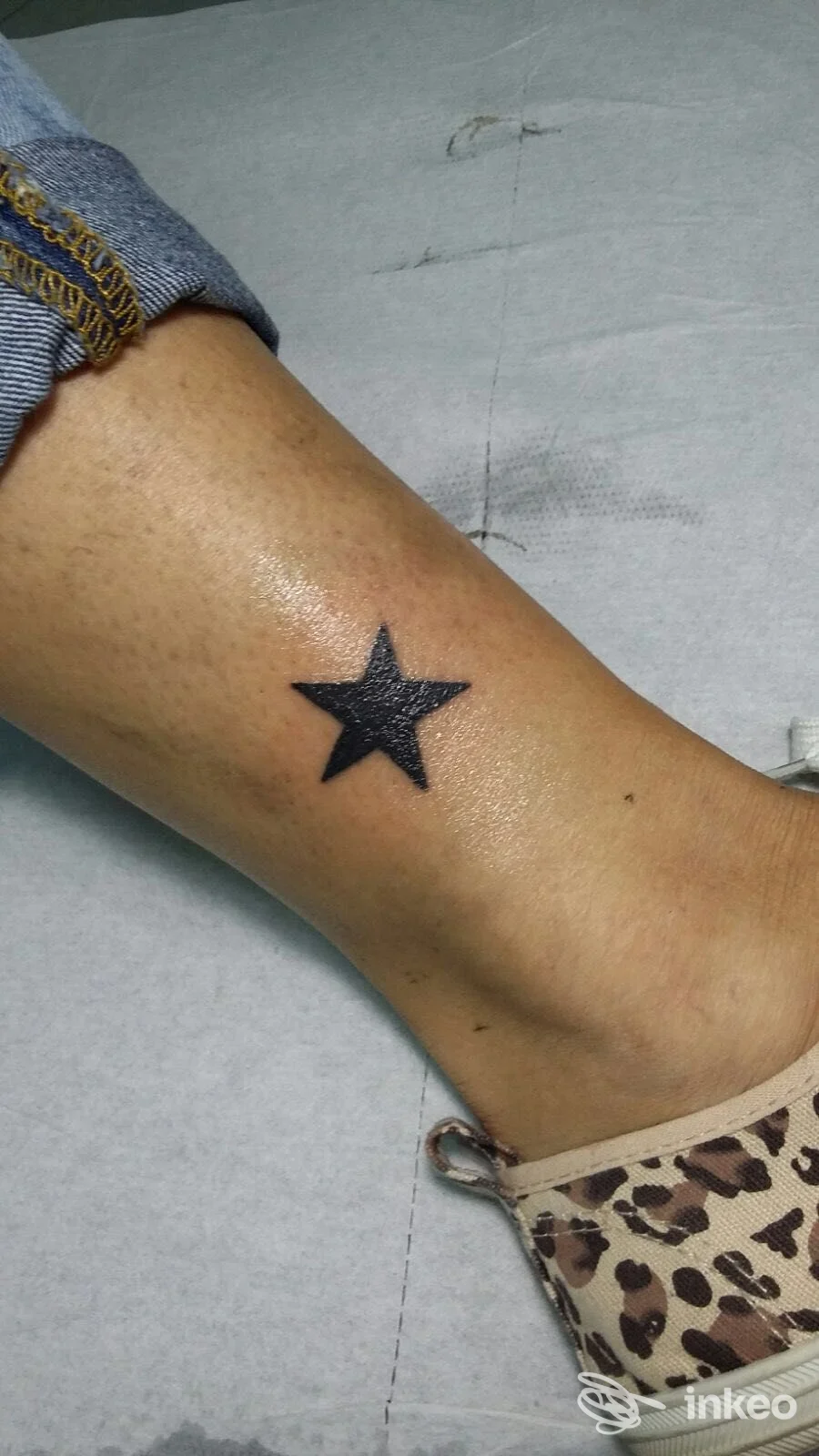 Primo piano di una piccola stella nera tatuata sulla caviglia, pelle visibile e scarpa con fantasia; immagine fornita dallo studio Tattoo time a Sciacca.