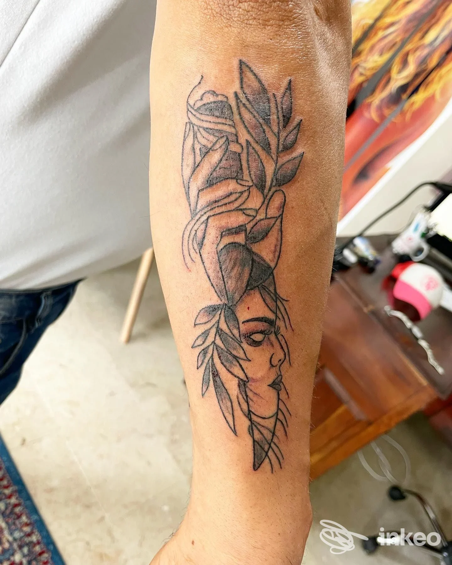 Tatuaggio in bianco e nero su avambraccio: mano, volto stilizzato e foglie. Tatuaggi David Ink, Trapani.
