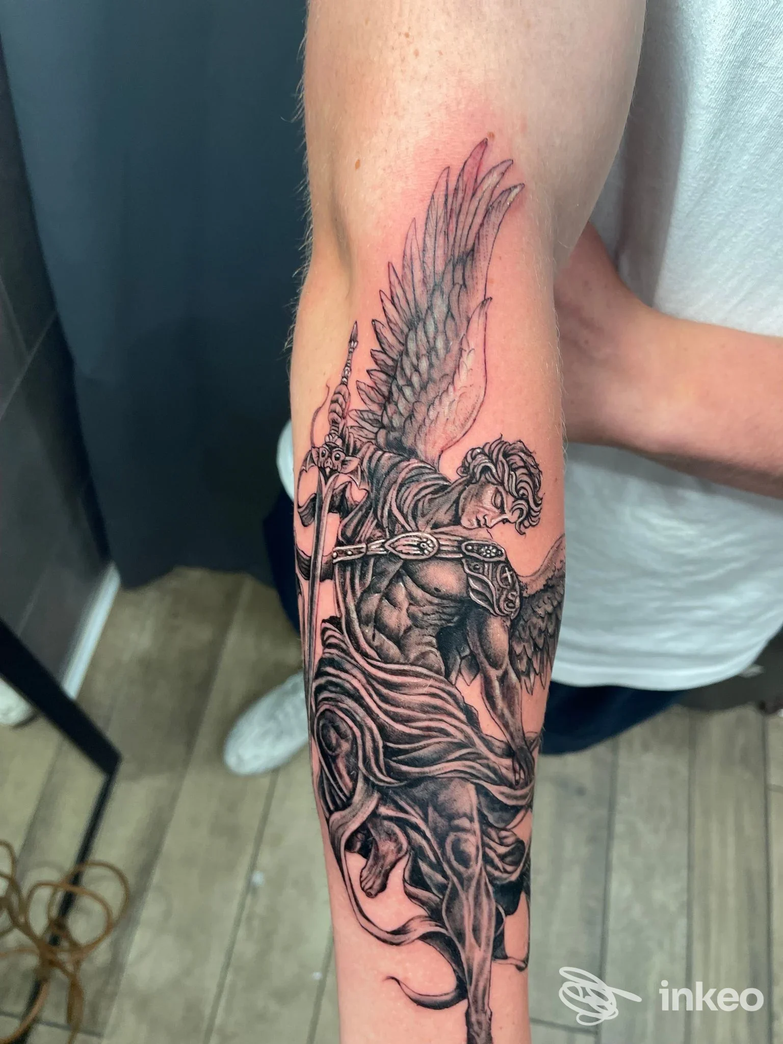 Tatuaggio in bianco e nero di un arcangelo alato sull'avambraccio, con dettagli realistici; foto da That's Amore Tattoo Studio, Palermo.