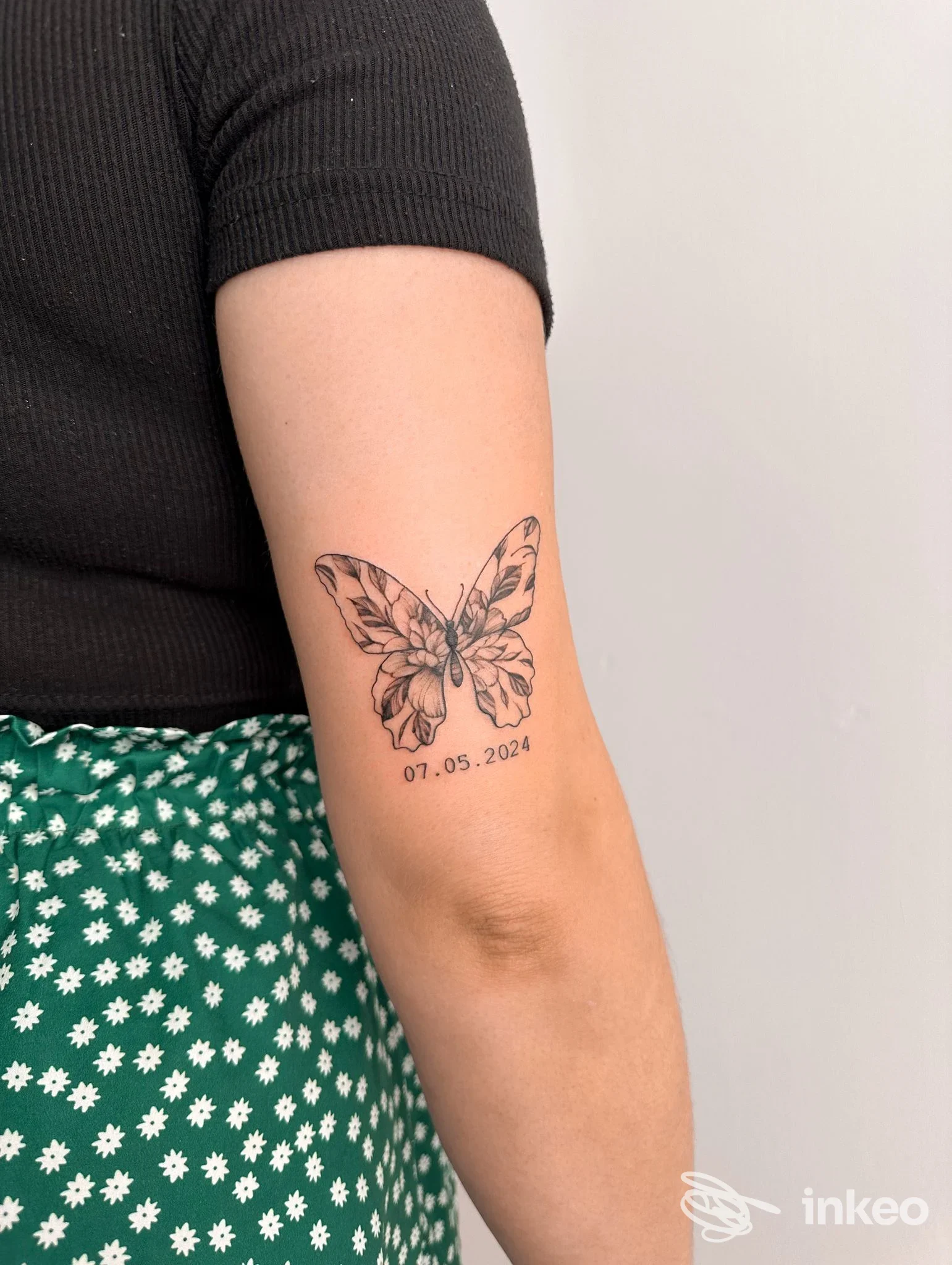 Farfalla tatuata in bianco e nero sul braccio superiore con data sottostante, immagine fornita da The Odyssey Tattoo, Trapani.