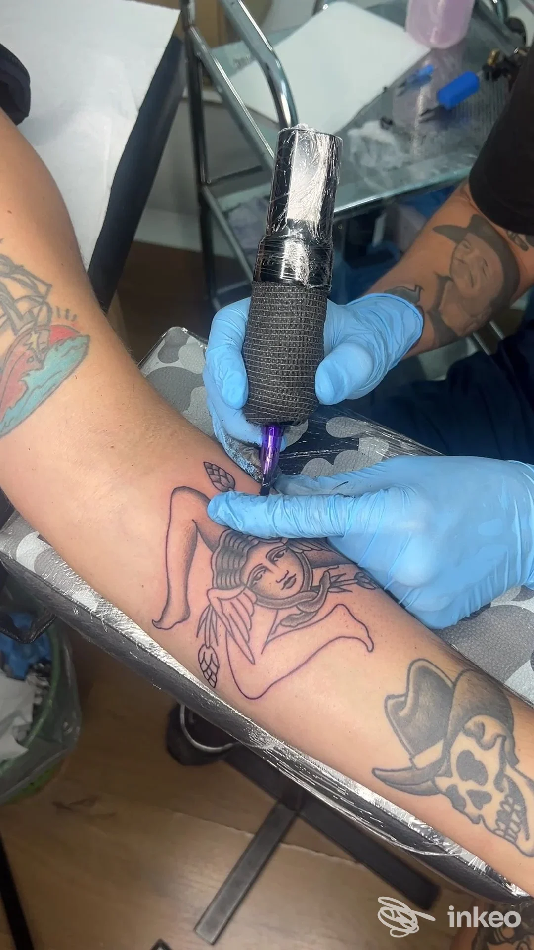 Tatuatore al lavoro sull'avambraccio a Catania: macchina per tatuaggi e disegno in corso presso The Travellers Tattoo, primo piano sulla mano.