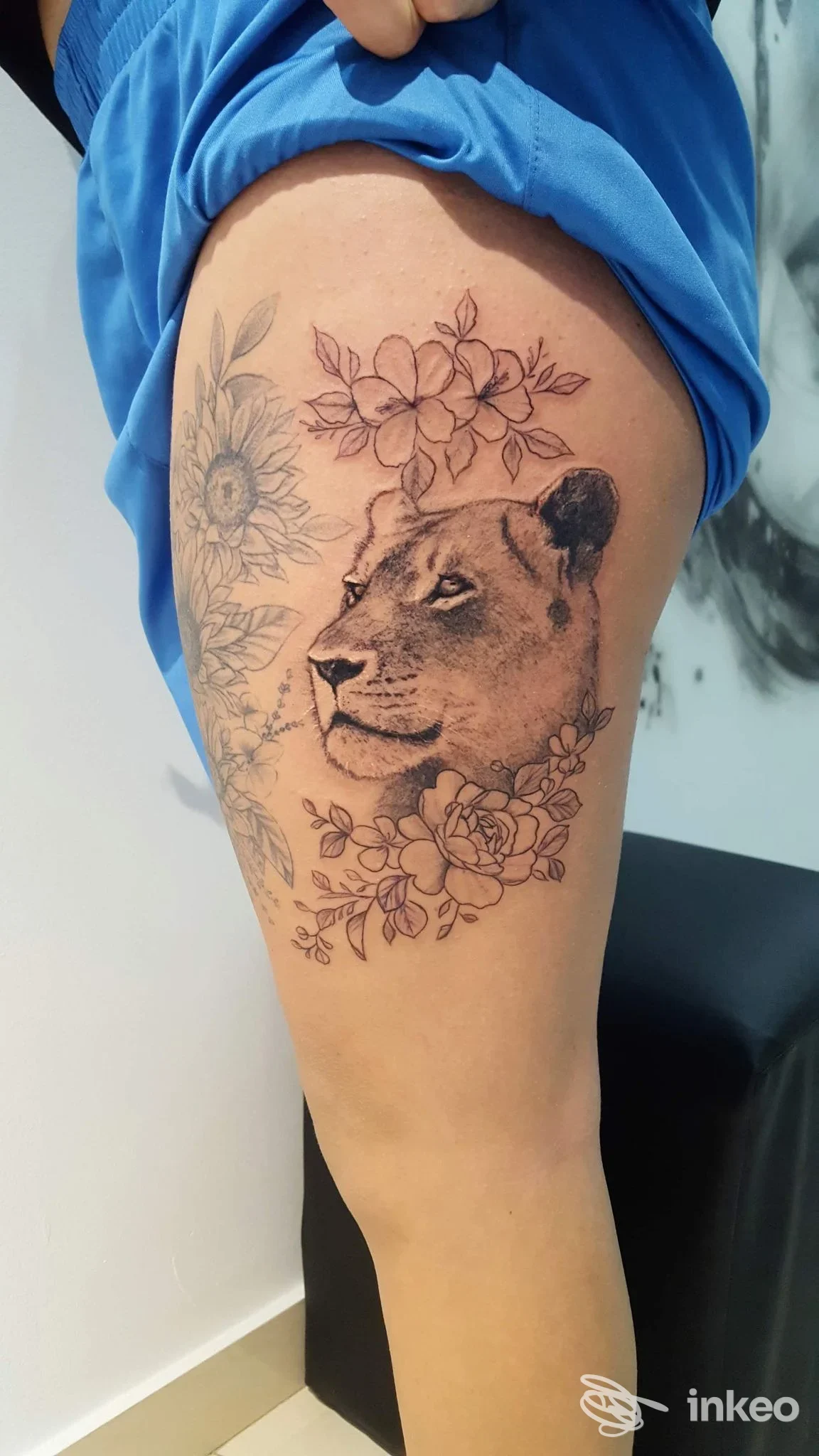 Tatuaggio realistico di testa di leonessa circondata da fiori sull'interno coscia, realizzato da Ttinko Studio Tattoo a Comiso.