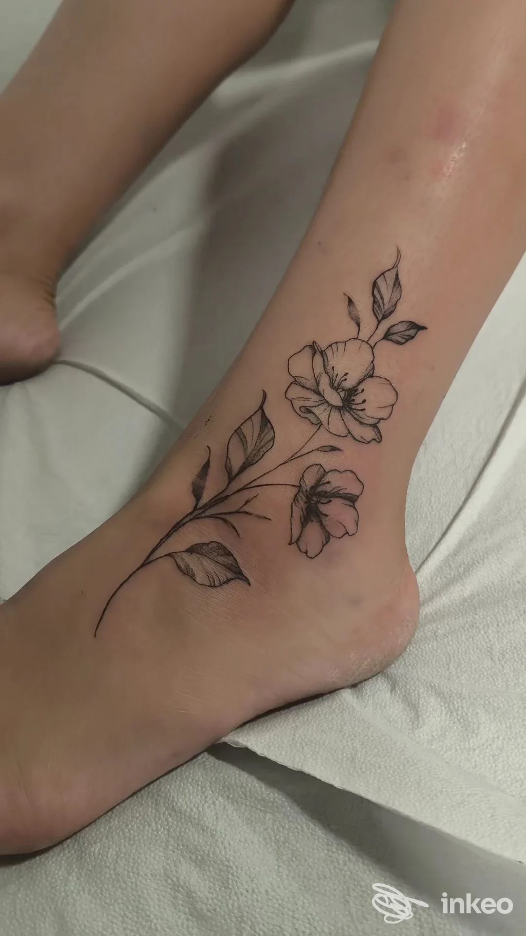 Tatuaggio floreale in bianco e nero sulla caviglia/piede, linea sottile e foglie, eseguito da sINKronize Tattoo a Catania.
