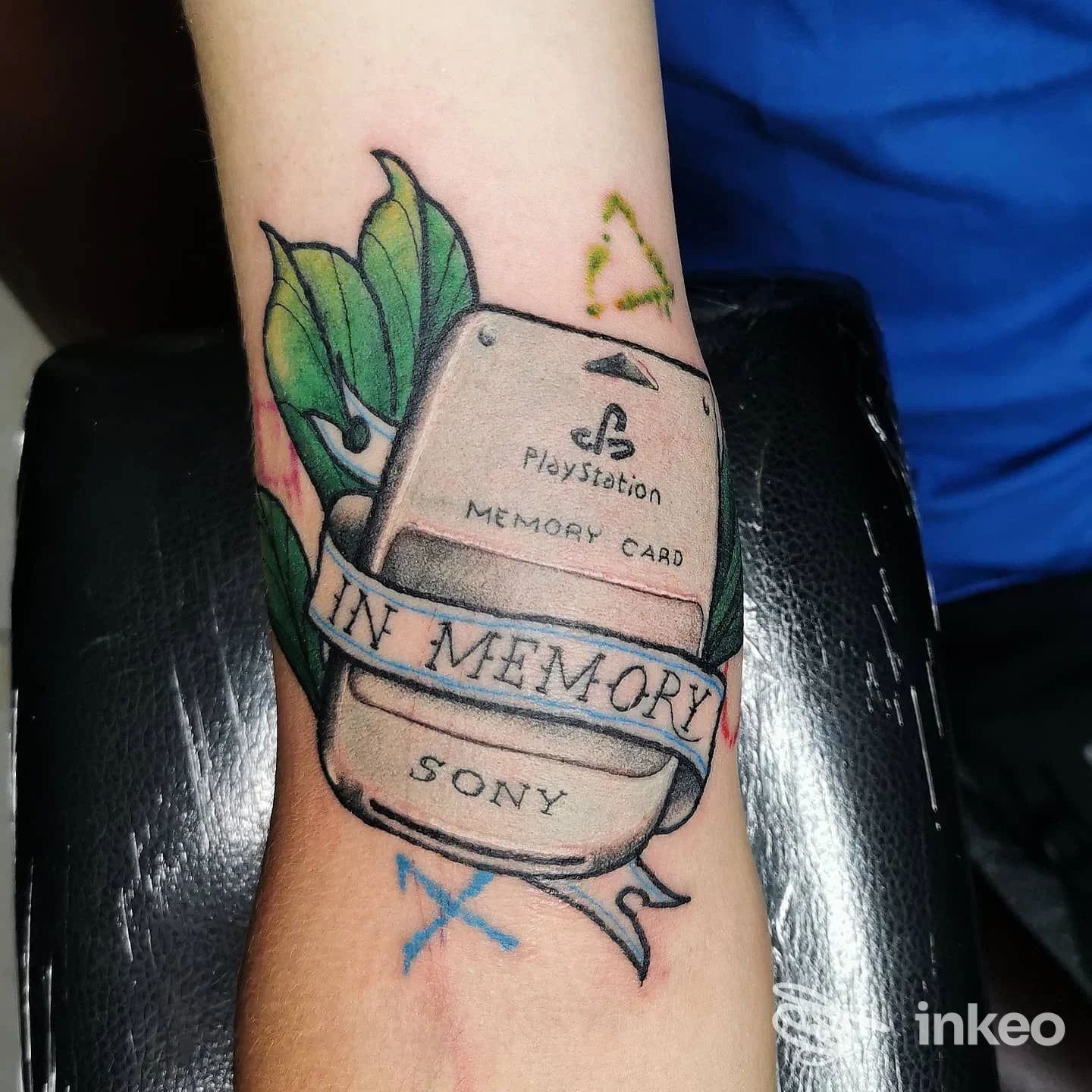 Tatuaggio di una memory card PlayStation con nastri e foglie sull'avambraccio, realizzato da Absinthium Tattoo a Palermo.