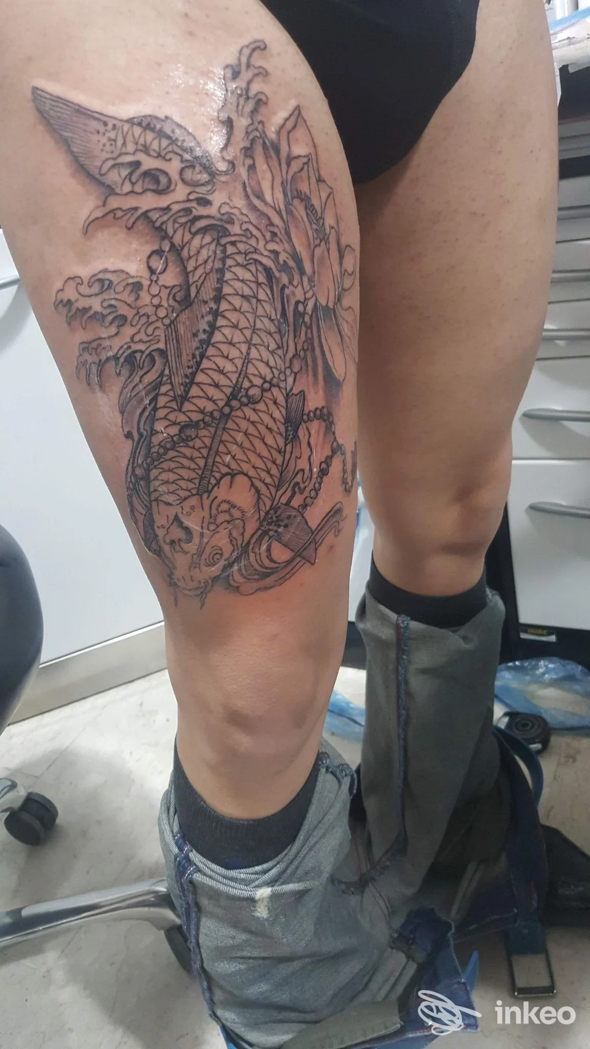 Tatuaggio a inchiostro nero a forma di pesce koi con onde sulla coscia, foto fornita da Egizio Tattoo, Palermo.