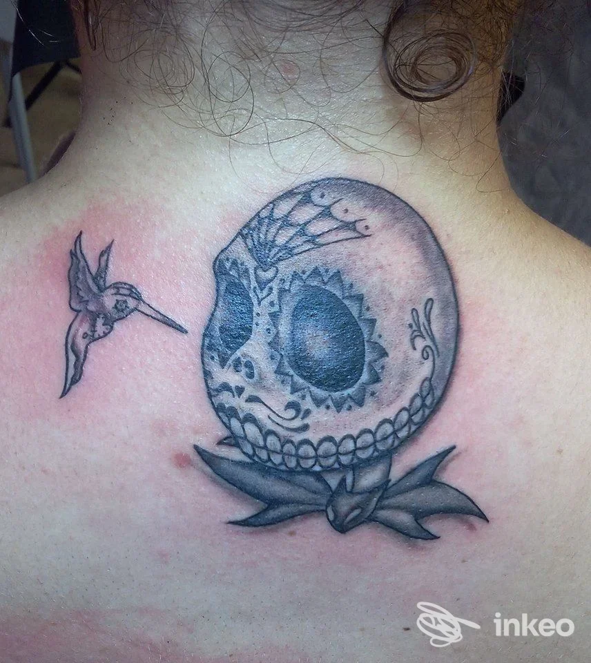 Tatuaggio in bianco e nero di teschio decorato e colibrì sulla nuca/parte alta della schiena — Bonnie & Clyde Tattoo, Palermo.