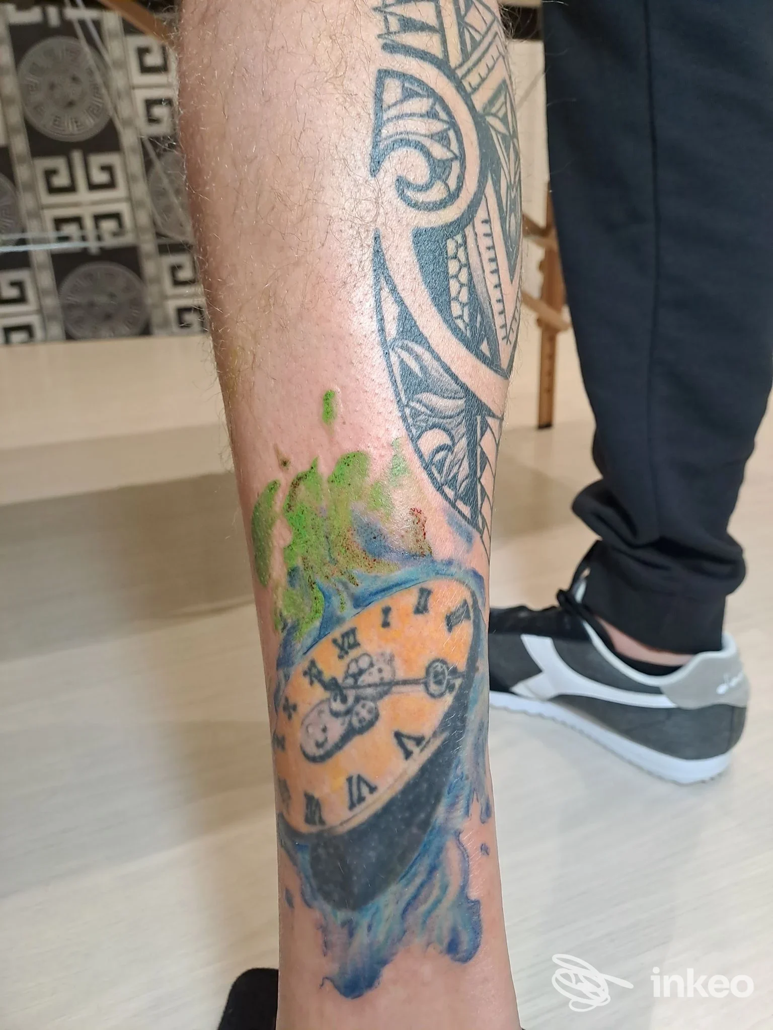 Foto del polpaccio con tatuaggi colorati che mostrano un orologio e motivi tribali, scattata per GMR Piercing e Tattoo a Santa Margherita di Belice.