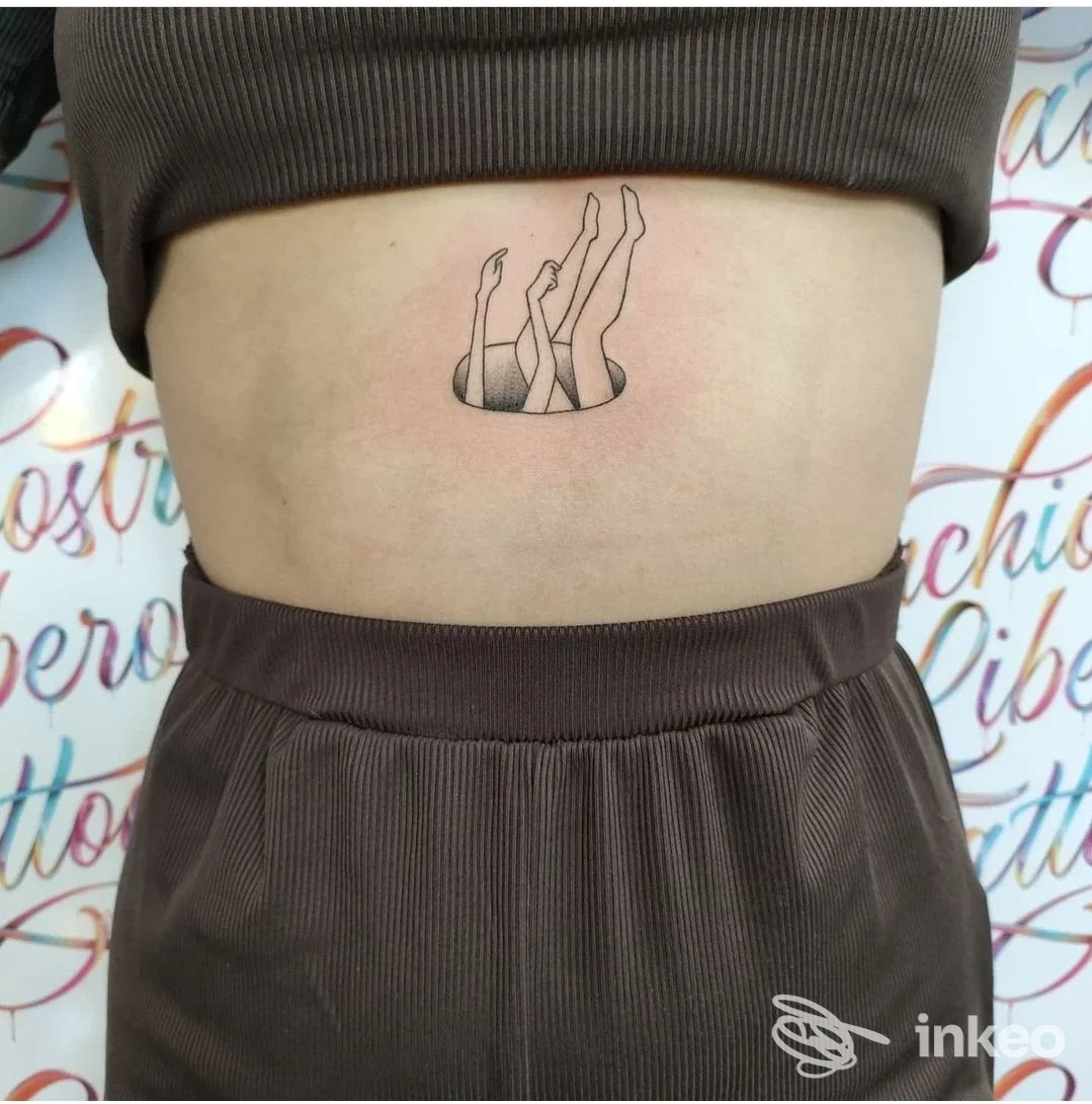 Tatuaggio minimal di gambe che emergono da un buco sull'addome, realizzato da Inchiostro Libero Studio Tattoo a Partinico.