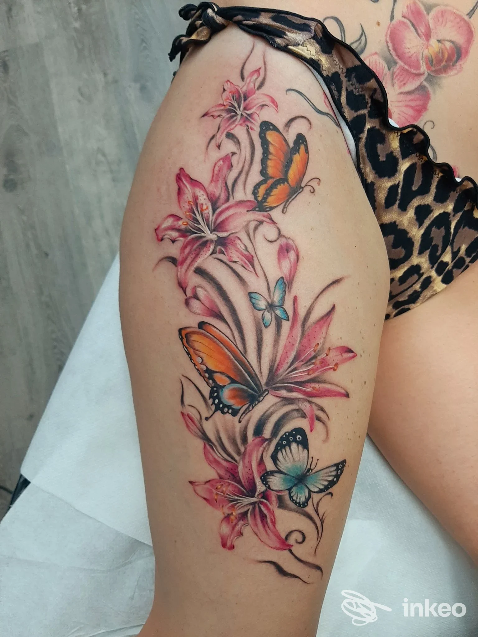Tatuaggio colorato di gigli e farfalle sulla coscia, eseguito da Ink Generation Tattoo a Ragusa.