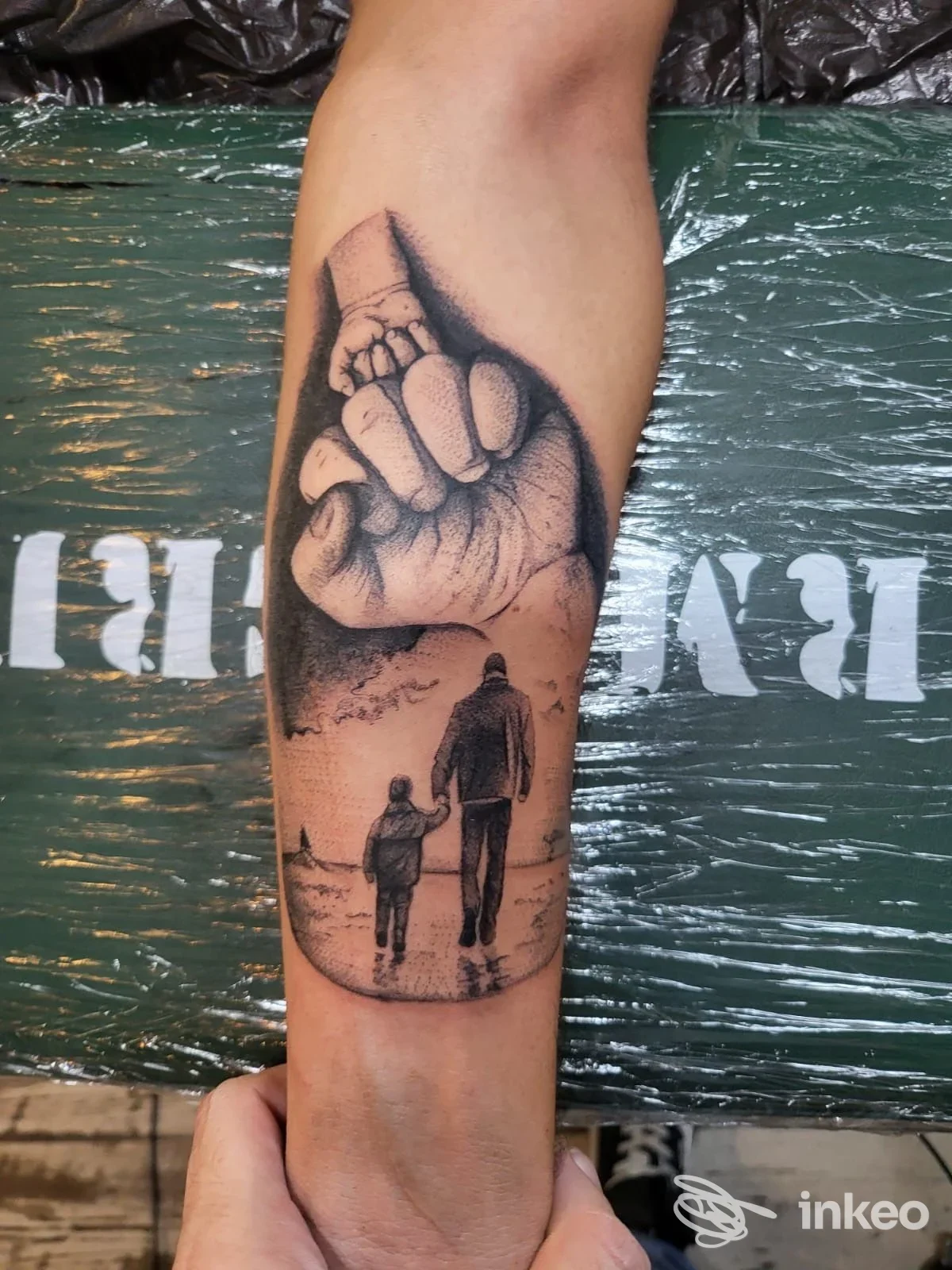 Tatuaggio in bianco e nero sull'avambraccio raffigurante una mano e due figure che camminano mano nella mano; VS Narashima Tattoo, Messina.