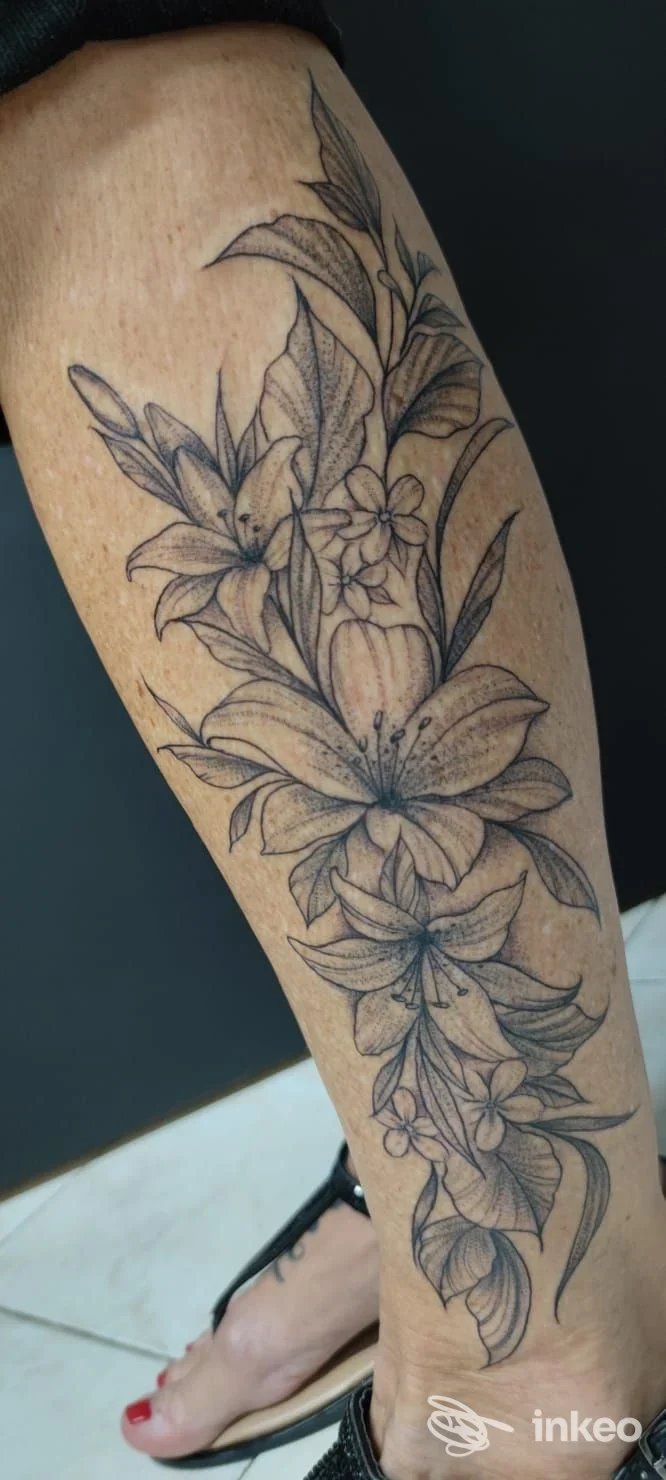 Tatuaggio floreale in bianco e nero sul polpaccio, dettaglio di gigli e foglie; lavoro eseguito presso World Art Tattoo, Caltagirone.