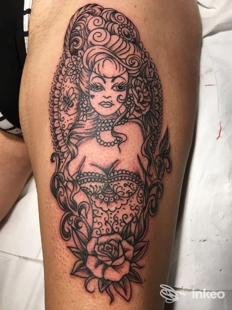 Tatuaggio in bianco e nero su coscia: figura femminile pin-up entro ovale ornamentale con rose, realizzato da Gigi Tattoo Artstudio, Marina di Carrara.