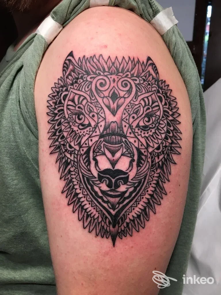 Grande tatuaggio stilizzato a forma di testa di lupo sul braccio superiore. Gigi Tattoo Artstudio, Marina di Carrara.