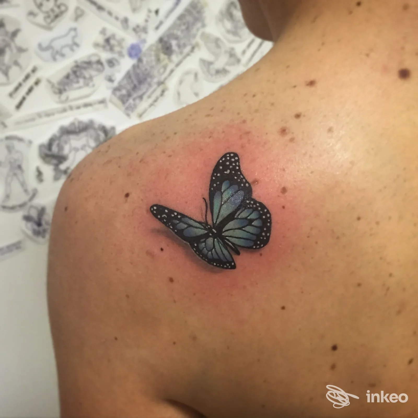 Tatuaggio a forma di farfalla blu e nera sulla spalla, eseguito da Hide and Seek • Tattoo Shop a Borgo San Lorenzo.