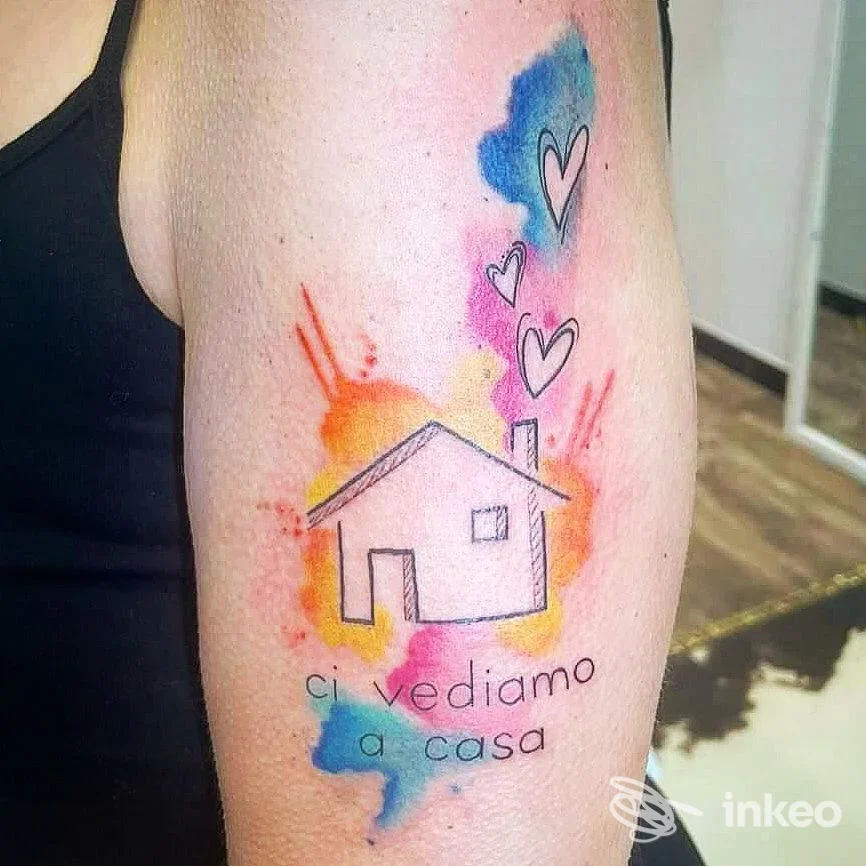 Tatuaggio acquerello di una casetta con cuori e la scritta “ci vediamo a casa” sul braccio. Hold the Line - Tattoo Shop, Livorno.