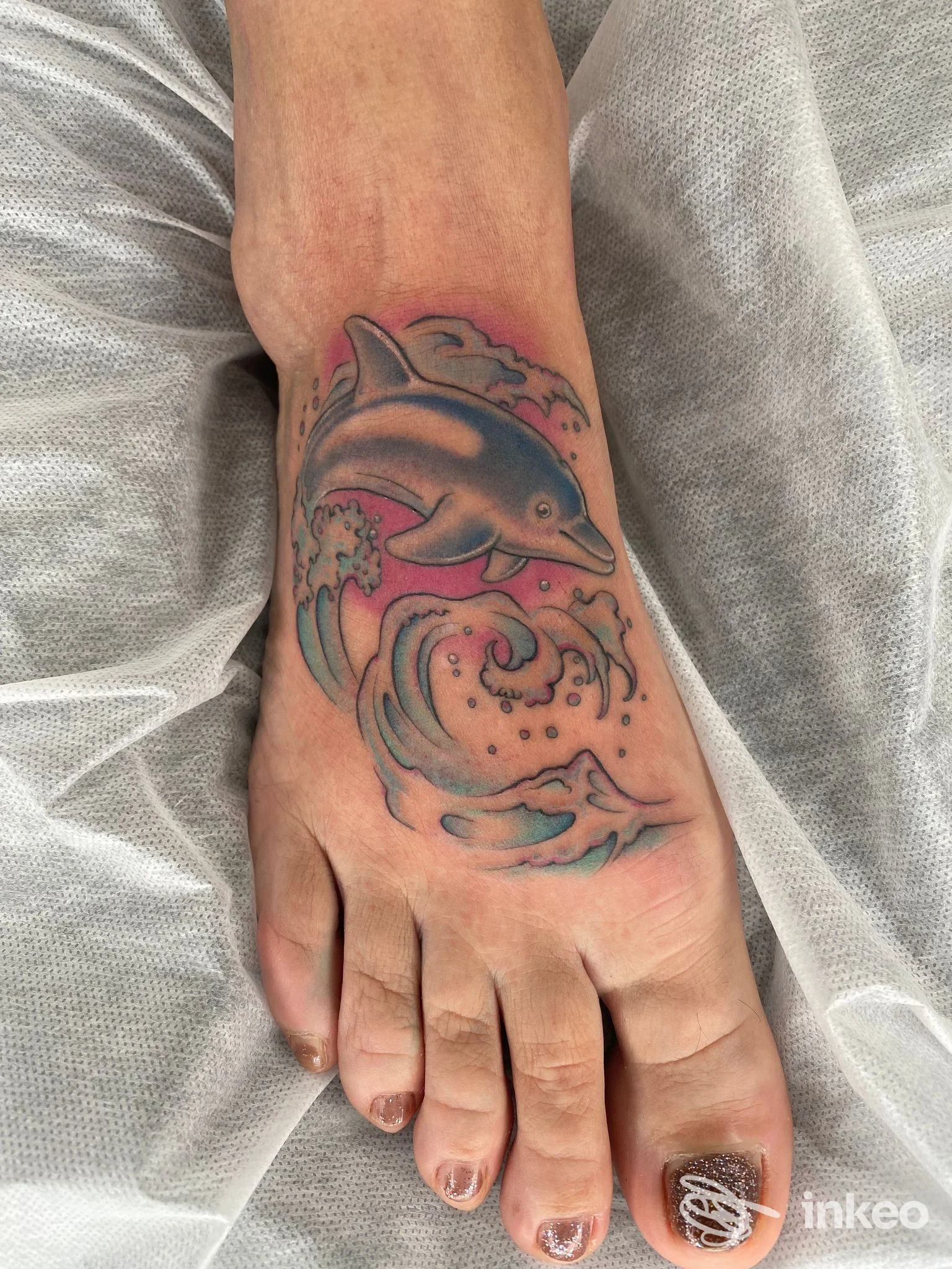 Tatuaggio a colori di un delfino tra onde sul dorso del piede, realizzato da INKSPIRITO TATTOO ad Arezzo.