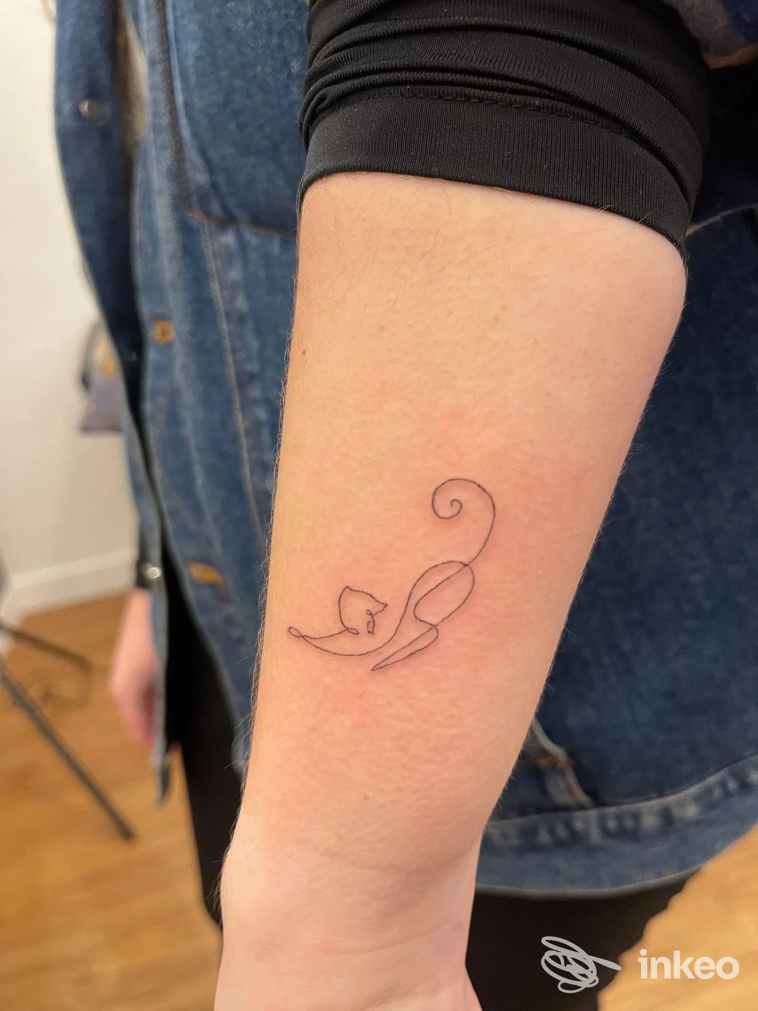 Tatuaggio lineare piccolo su avambraccio: figura stilizzata simile a un gatto. Foto scattata presso Ikigai Tattoo Studio, Firenze.