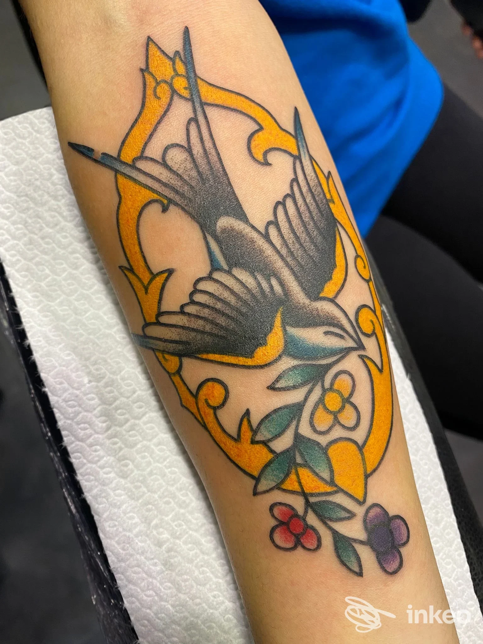 Tatuaggio tradizionale di rondine con rametto fiorito sull'avambraccio, con tocchi gialli e colori vivaci, realizzato da GIULS TATTOOER a Follonica.