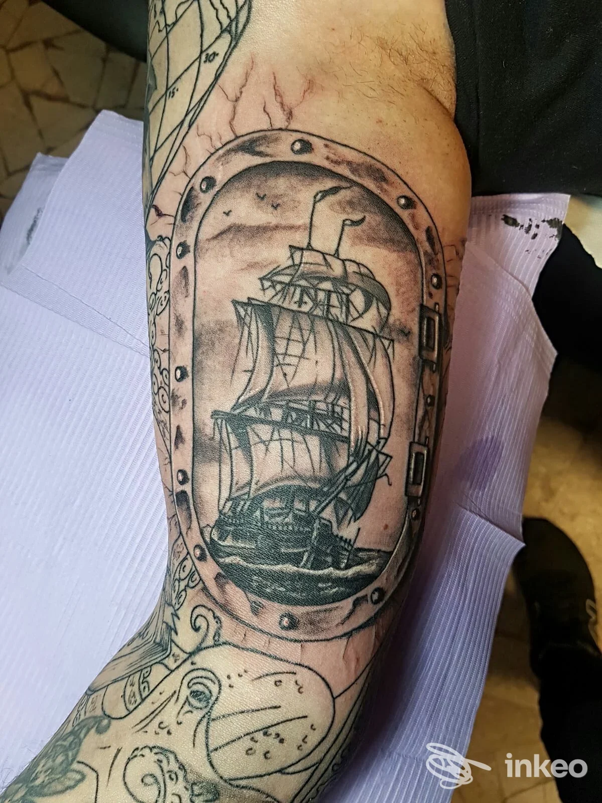 Tatuaggio su avambraccio con nave a vela incorniciata da un oblò, lavoro in bianco e nero. La Sartoria Tattoo, Colle di Val d'Elsa.